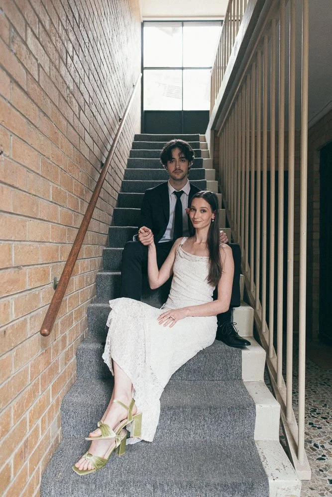 , BRIDE AND GROOM CASUALLY POSING AT AN APARTMENT NEXT TO STAIRCASES WITH A ONE POINT PERSPECTIVE WHILE SITTING ON THE STAIRCASES