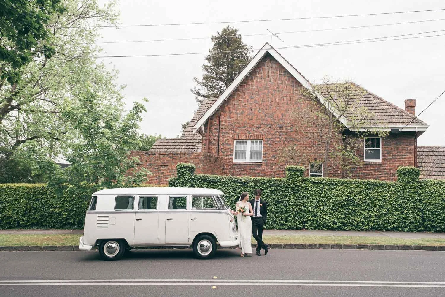 MELBOURNE  EDITORIAL WEDDING PHOTOGRAPHY, BRIDE AND GROOM POSING NEXT TO A OLD SCHOOL VW KOMBI VAN, WIDE ANGLE SHOT WITH A BRICK HOUSE BEHIND THEM