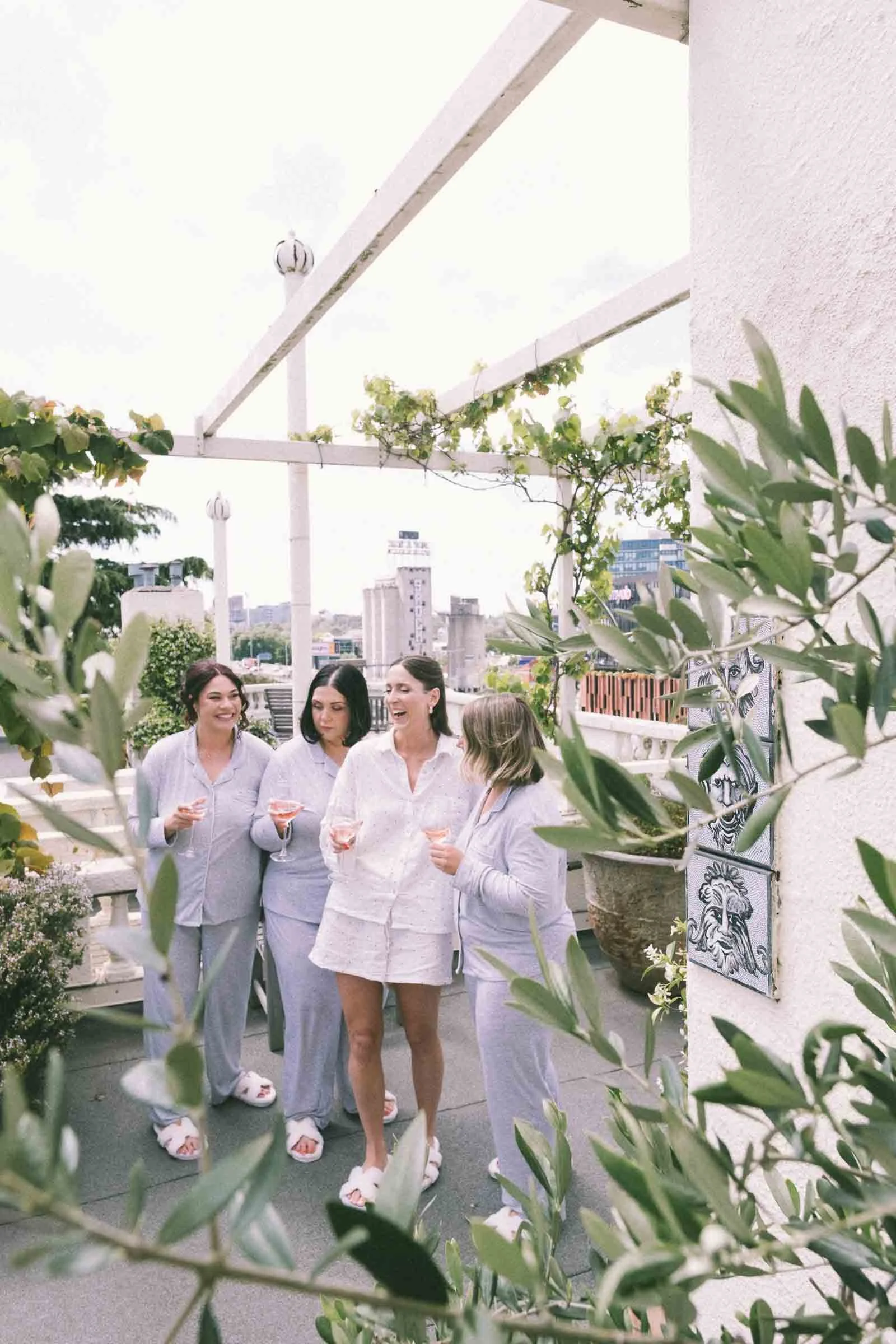 MELBOURNE BOTANICAL GARDEN WEDDING, BRIDE AND HER BRIDESMAIDS HAVING A DRINK AND GOING CHEERS ON THE BALCONY OVERLOOKING THE BEAUTIFUL MELBOURNE CITY