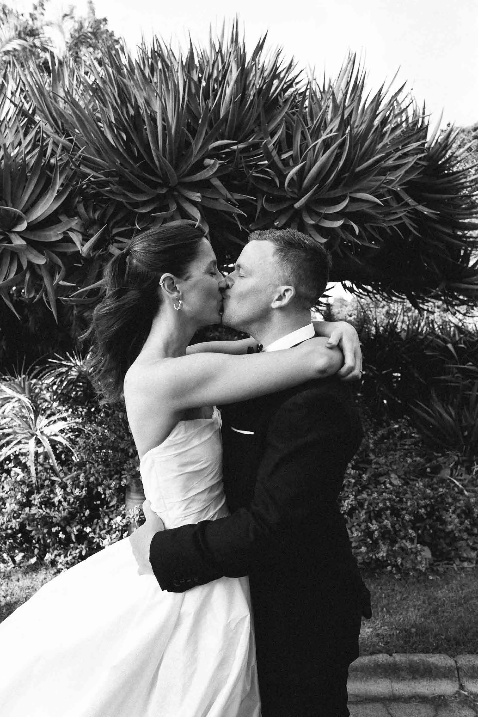 MELBOURNE BOTANICAL GARDEN WEDDING, BRIDE AND GROOM POSING ON THE GARDEN LAWNS, A BLACK AND WHITE PHOTO OF THEM KISSING