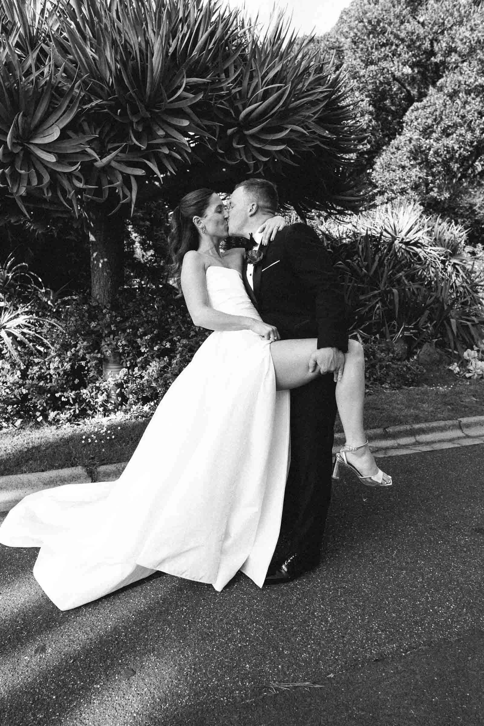 MELBOURNE BOTANICAL GARDEN WEDDING, BRIDE AND GROOM POSING ON THE GARDEN LAWNS, A BLACK AND WHITE PHOTO OF THEM KISSING, A CLASSING TIMELESS LEANING KISS
