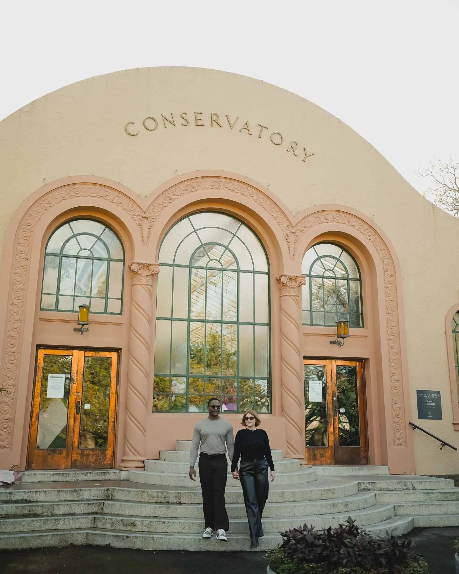 People standing on steps in front of the Fresno Yosemite International Conservatory, a pink building with large arched windows and ornate architectural details.