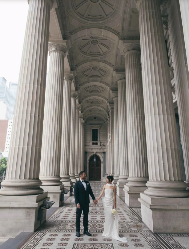 The Ultimate Old Treasury Building Wedding Guide, A couple holding hands between the huge columns of the Parliament Building In Melbourne