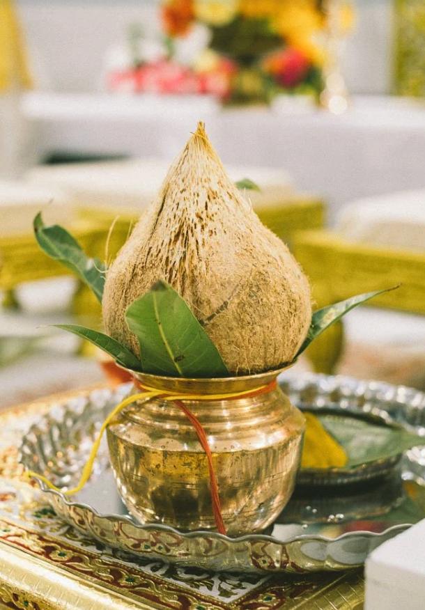 A ceremonial coconut placed on a golden bowl with green leaves around it, set on an ornate tray during a religious or cultural ritual.