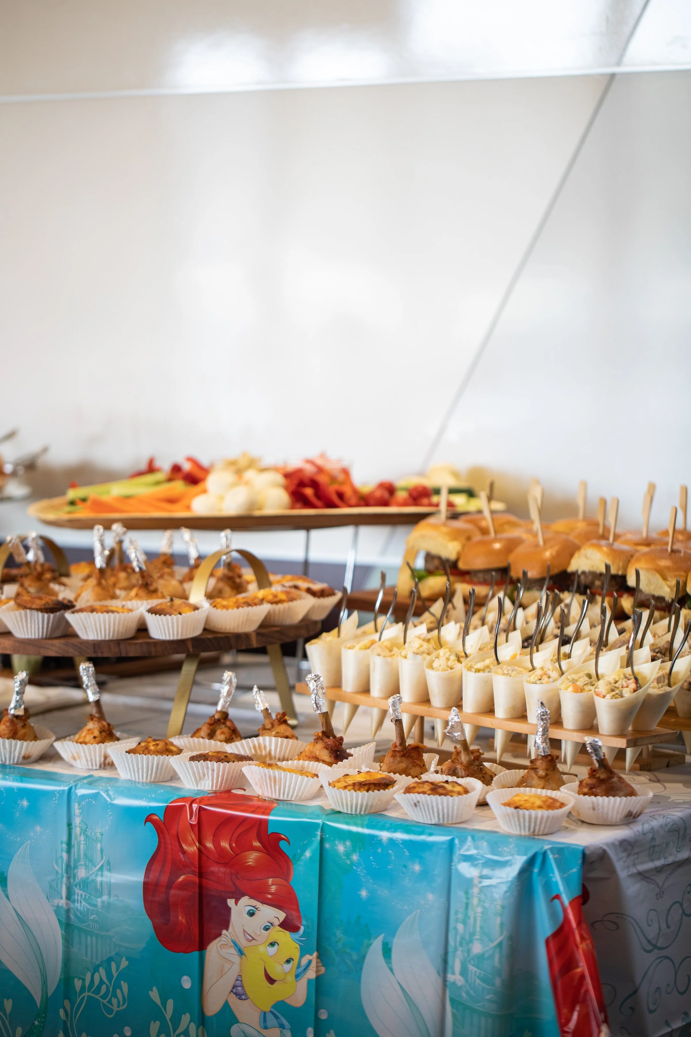 A table filled with various party foods, decorated with aDisney princess theme featuring Ariel and other princesses.