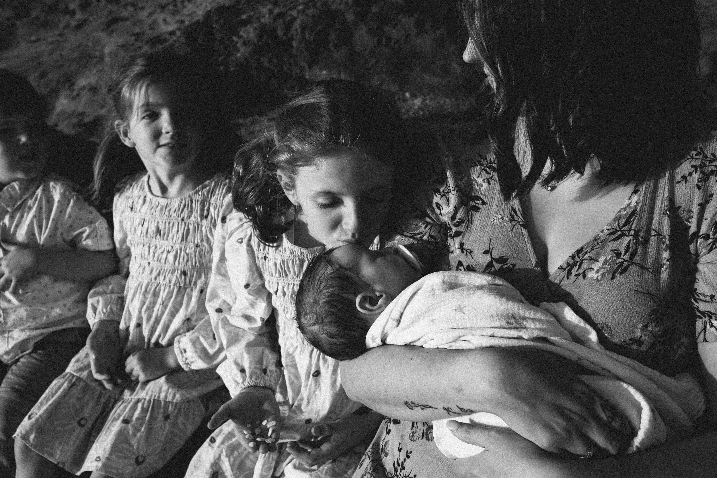 Black and white photo of a woman and five children, all lying close together on a soft surface, with the children resting their heads on the woman's arm and shoulder, appearing to be sleeping or resting, in a cozy and intimate setting.