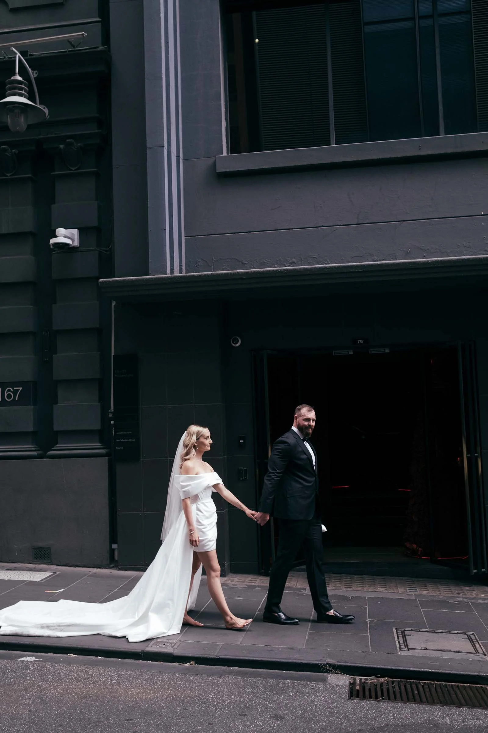 WEDDING COUPLE TAKING A STROLL THROUGH MELBOURNE LANEWAYS,  A DARK AND MOODY IMAGE WITH A MODERN FEEL WITH THE BRIDE DRESSED IN AN EXQUISITE DRESS