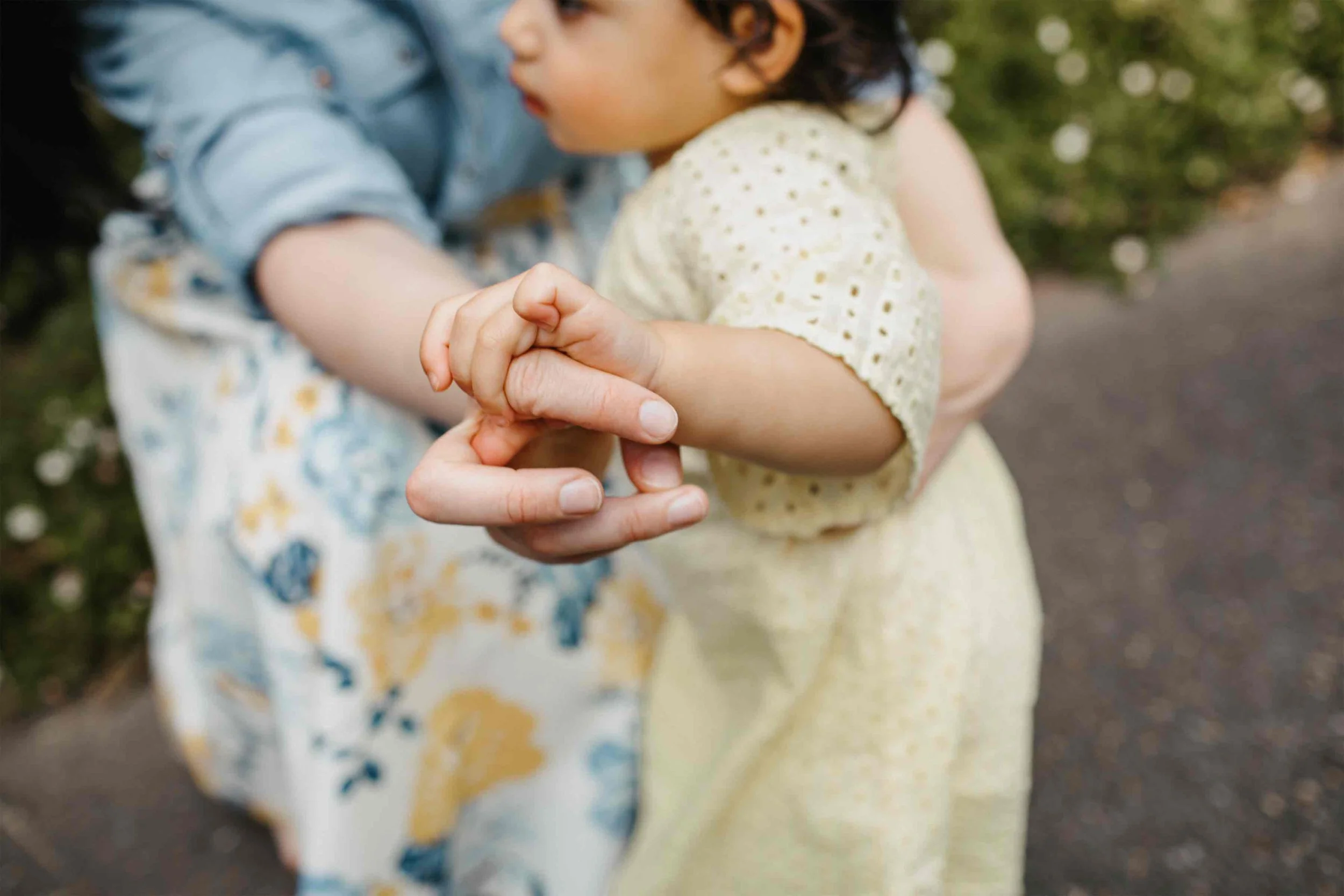 Two children holding hands outdoors, blurred background of greenery and a pathway.