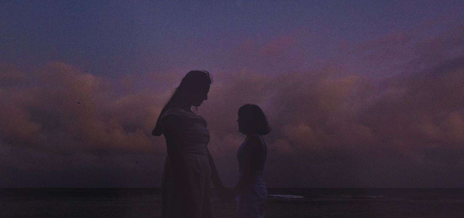 Intimate Melbourne Elopements for LGBTQ+ Couples, A SILHOUETTE OF A FEMALE COUPLE AT THE BEACH AT DUSK WITH BEAUTIFUL BLUE LIGHT AND GOLDEN CLOUDS IN THE BACKGROUND