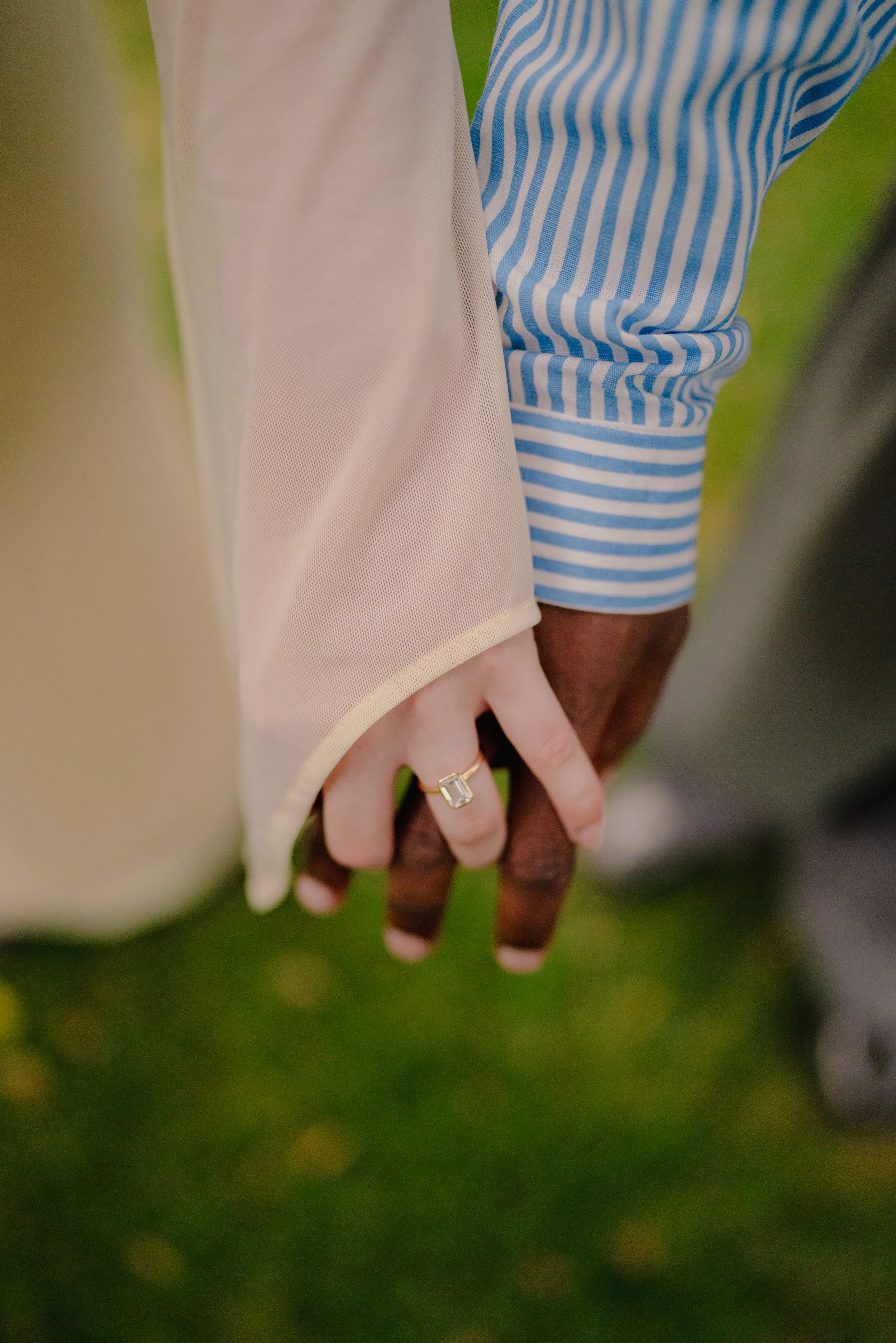 Close-up of two people holding hands, one person wearing a striped blue and white shirt and the other wearing a beige or cream long-sleeved top.