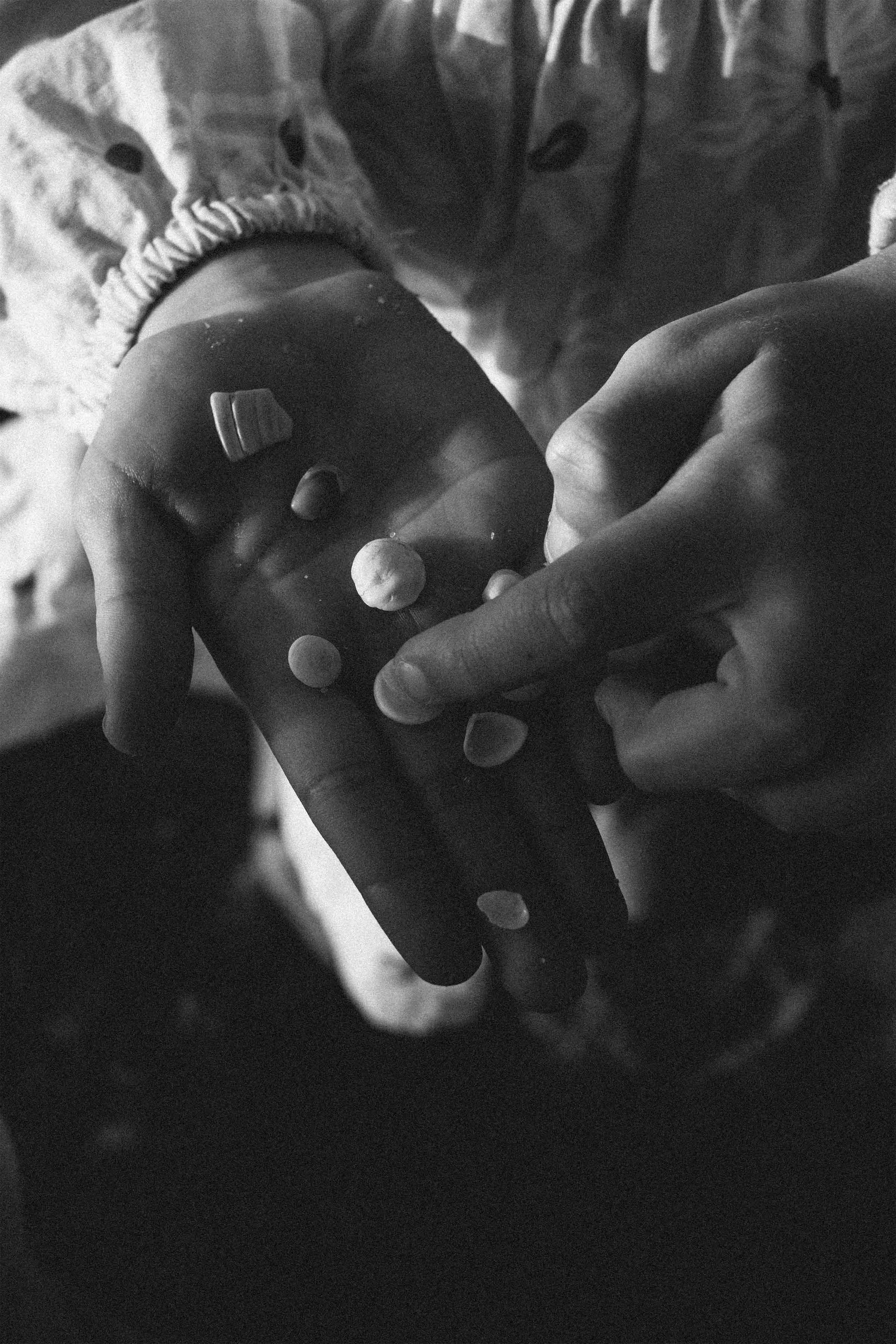 Close-up of a hand holding a game controller with small round objects on it, person wearing patterned clothing and a bracelet, in grayscale.