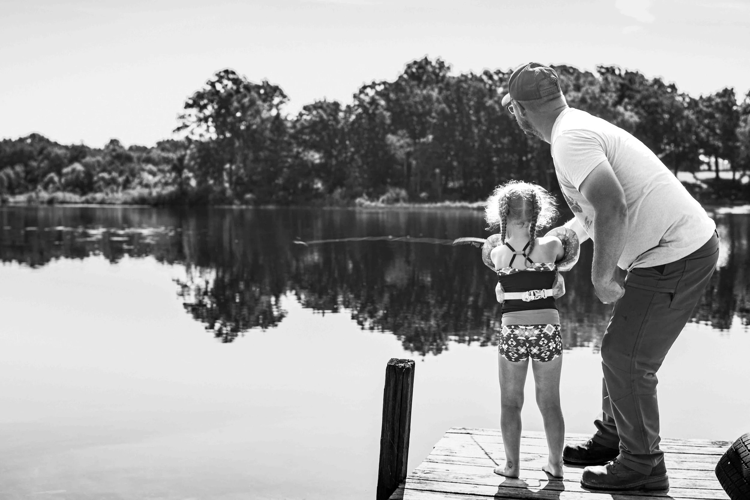 Heartfelt black and white photo of a dad teaching his daughter to fish, part of a documentary family photography session by Forever Ago Photography in Jerome Michigan