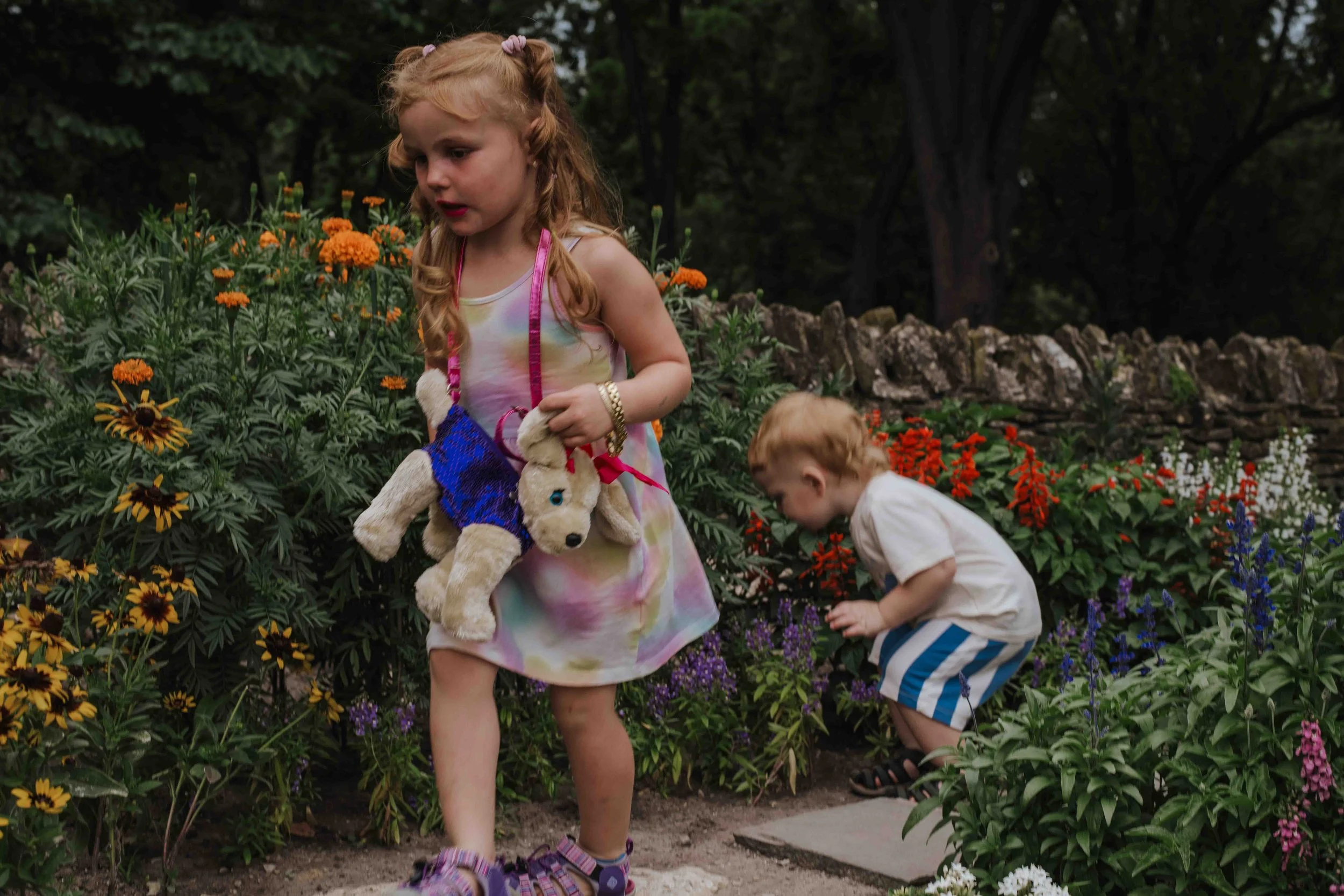 Candid moment of siblings skipping through a garden and stopping to smell the flowers, highlighting the magic of childhood during a family photography session by Forever Ago Photography in Dearborn Michigan