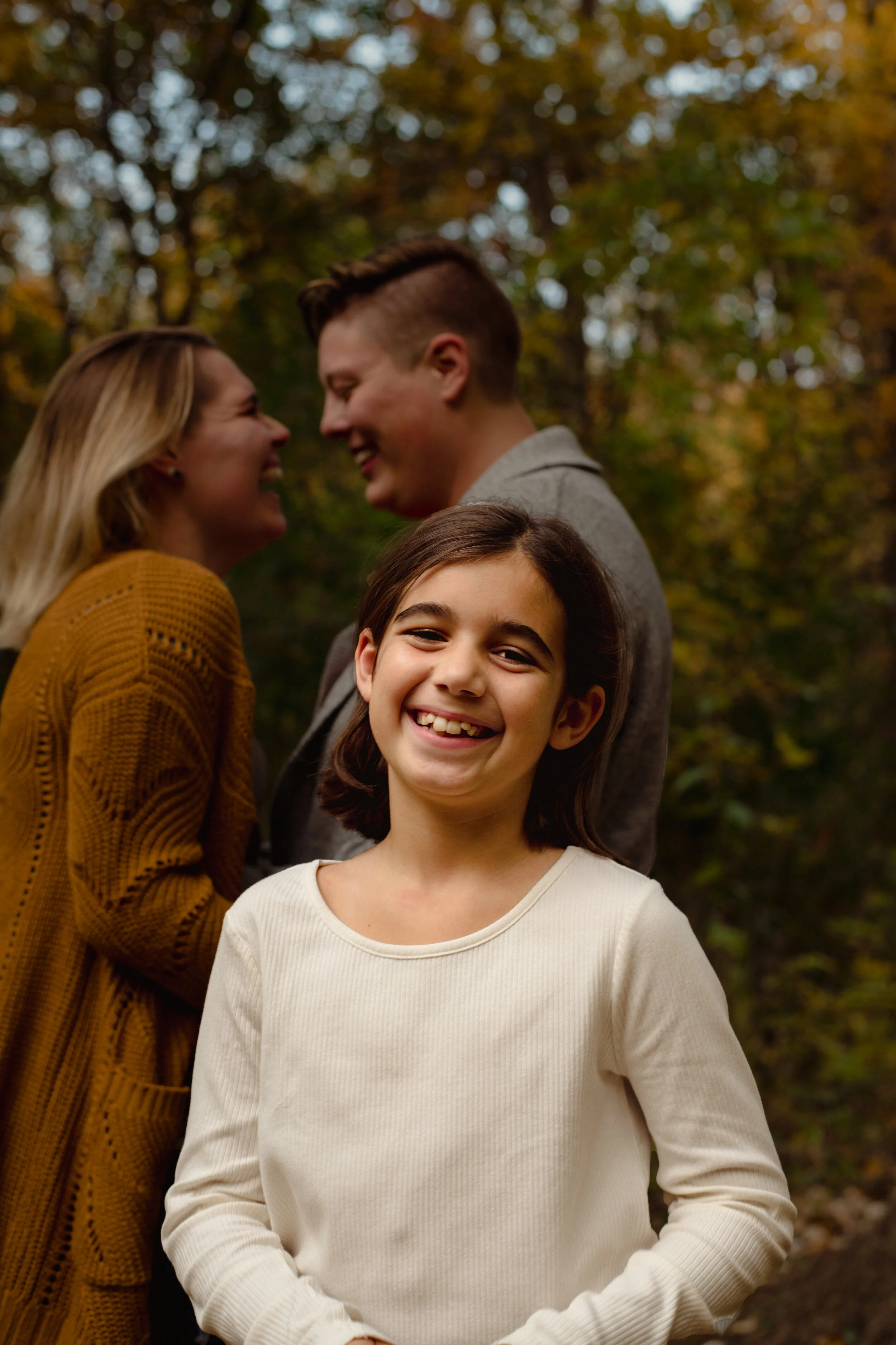 Heartwarming candid image of parents sharing a kiss while their daughter looks on during a fall family photography session by Forever Ago Photography in Washtenaw County Michigan