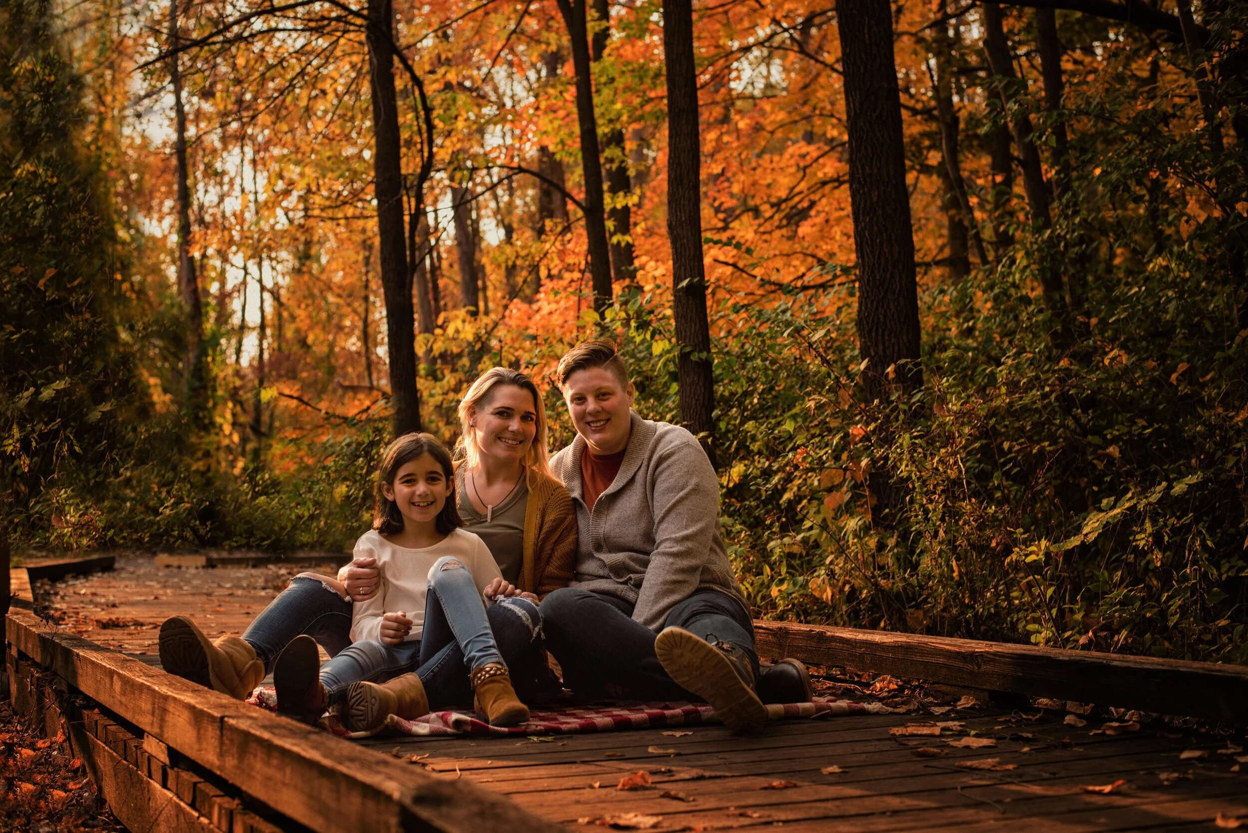 Heartwarming photo of partners with their child surrounded by colorful fall leaves during a family photography session by Forever Ago Photography. Capturing authentic family moments and the beauty of autumn in Ann Arbor Michigan