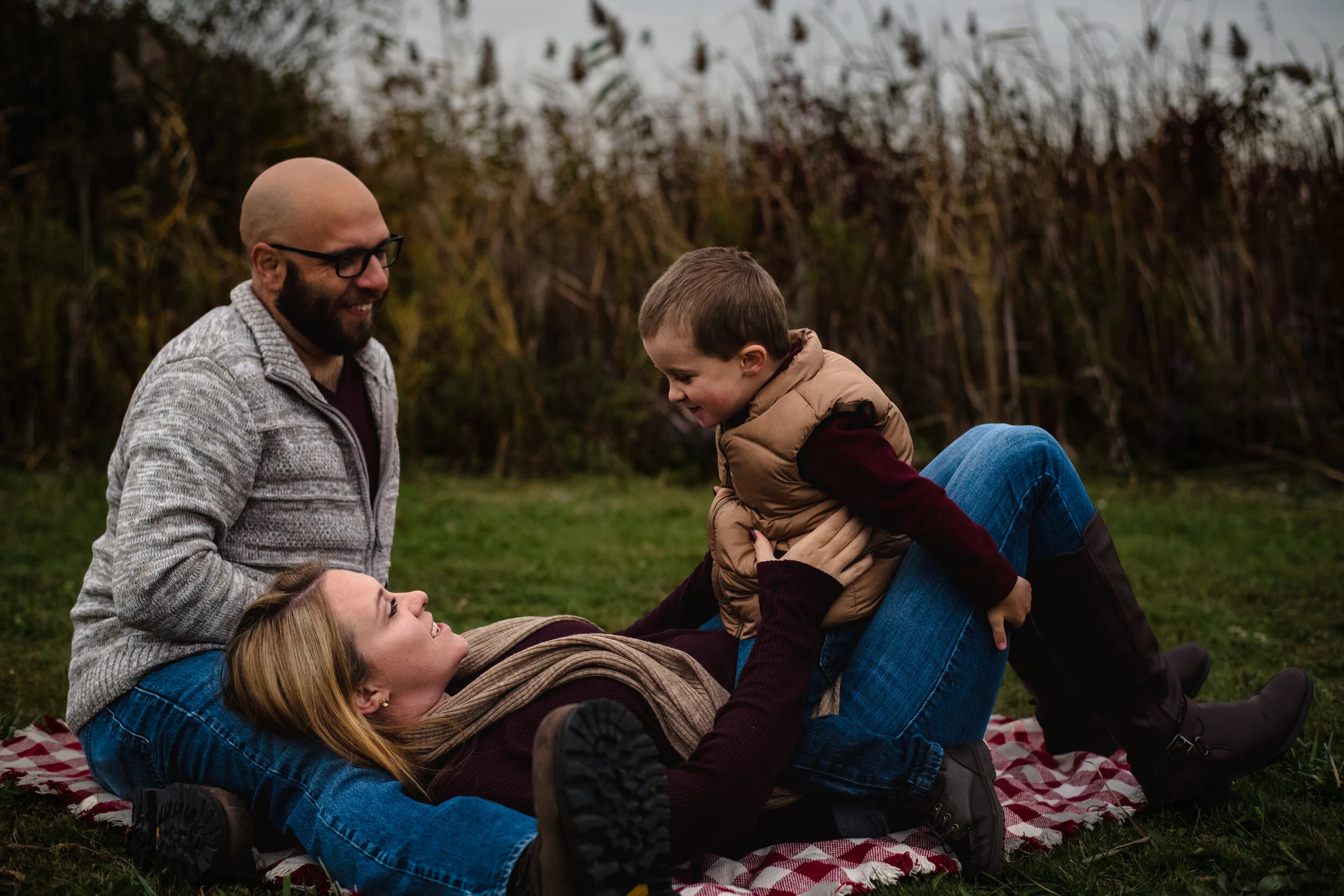 Candid photo of parents with their son on a picnic blanket during a family photography session by Forever Ago Photography. Capturing warm, authentic family moments in a natural outdoor setting in Wayne County Michigan