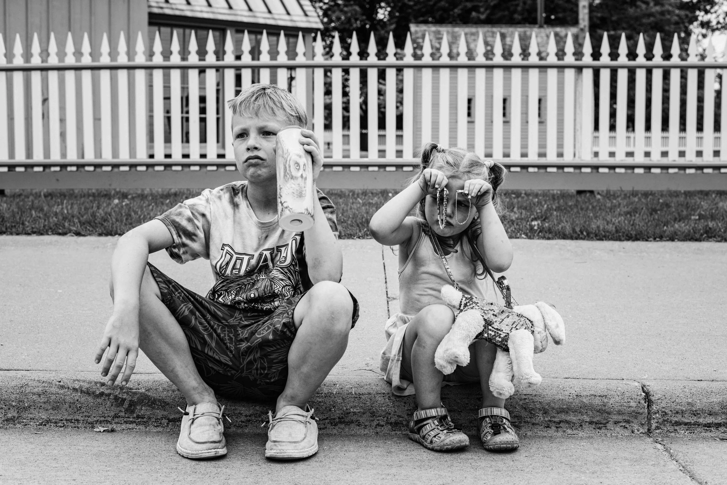 Black and white candid photo of brother and sister sitting on a curb at Greenfield Village during a family photography session by Forever Ago Photography. Capturing authentic sibling moments and timeless memories at Greenfield Village Southeast Michi