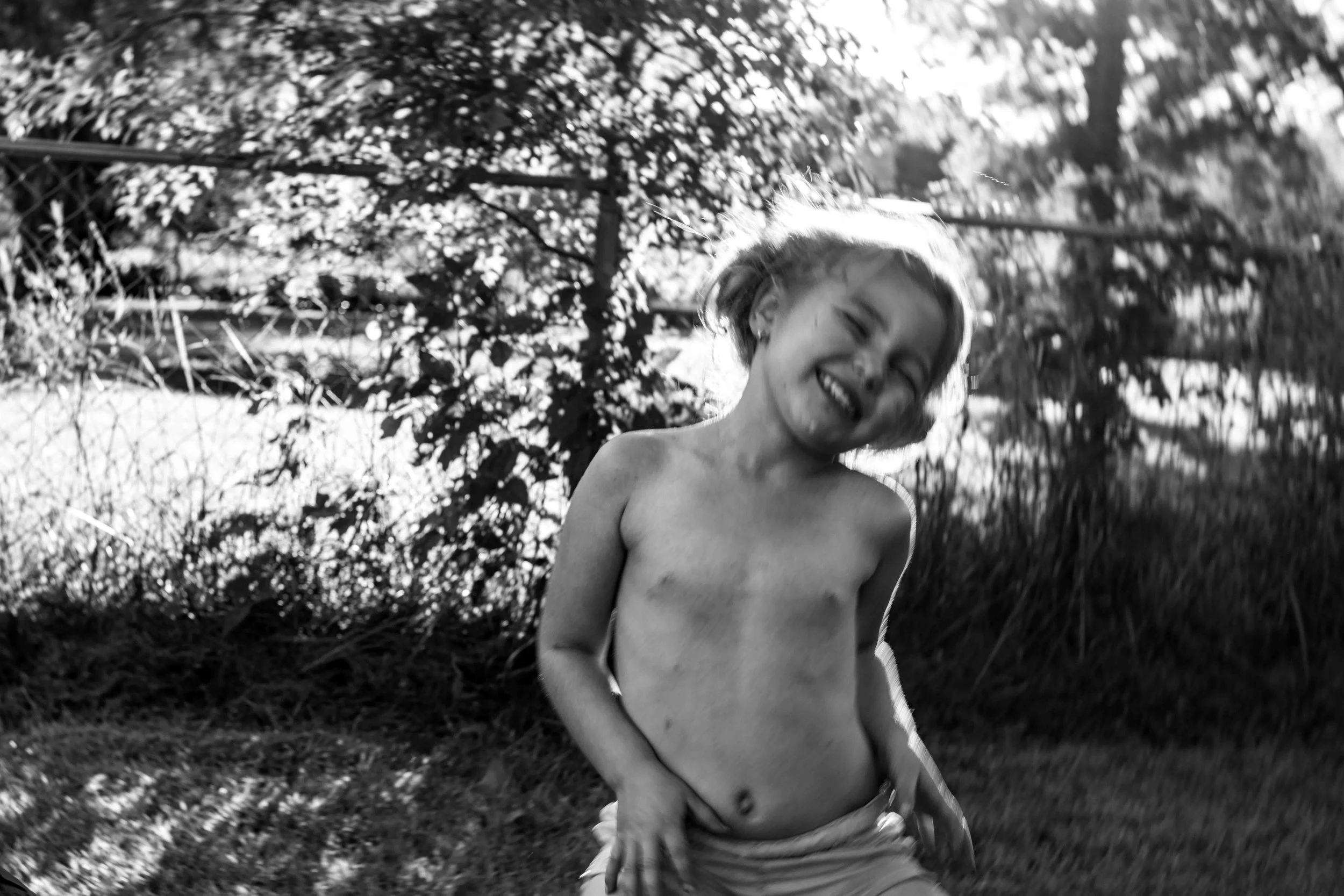 Black and white candid photo of a girl joyfully dancing in the summer sun during a documentary-style family photography session by Forever Ago Photography. Capturing carefree childhood moments and authentic joy in Monroe Michigan