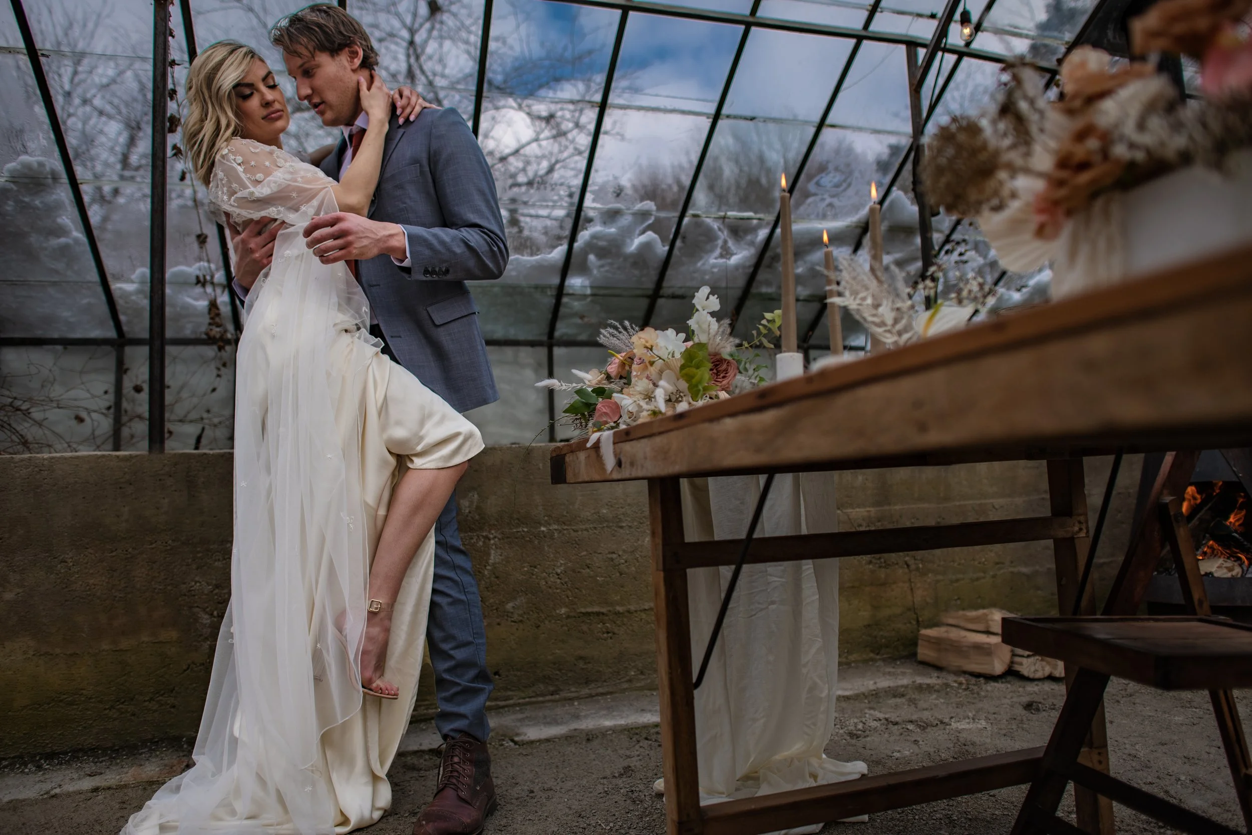 Dreamy image of a groom dipping his bride for a kiss, surrounded by greenery in a winter wedding greenhouse setting, captured by Forever Ago Photography in Trenton Michigan