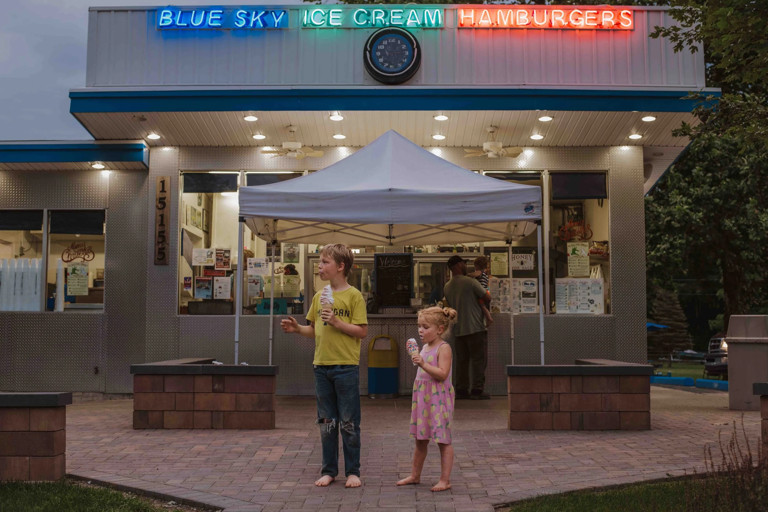 Joyful candid photo of children savoring ice cream on a summer afternoon outside a parlor, captured by Forever Ago Photography. Celebrating the sweetness of childhood in New Boston Michigan