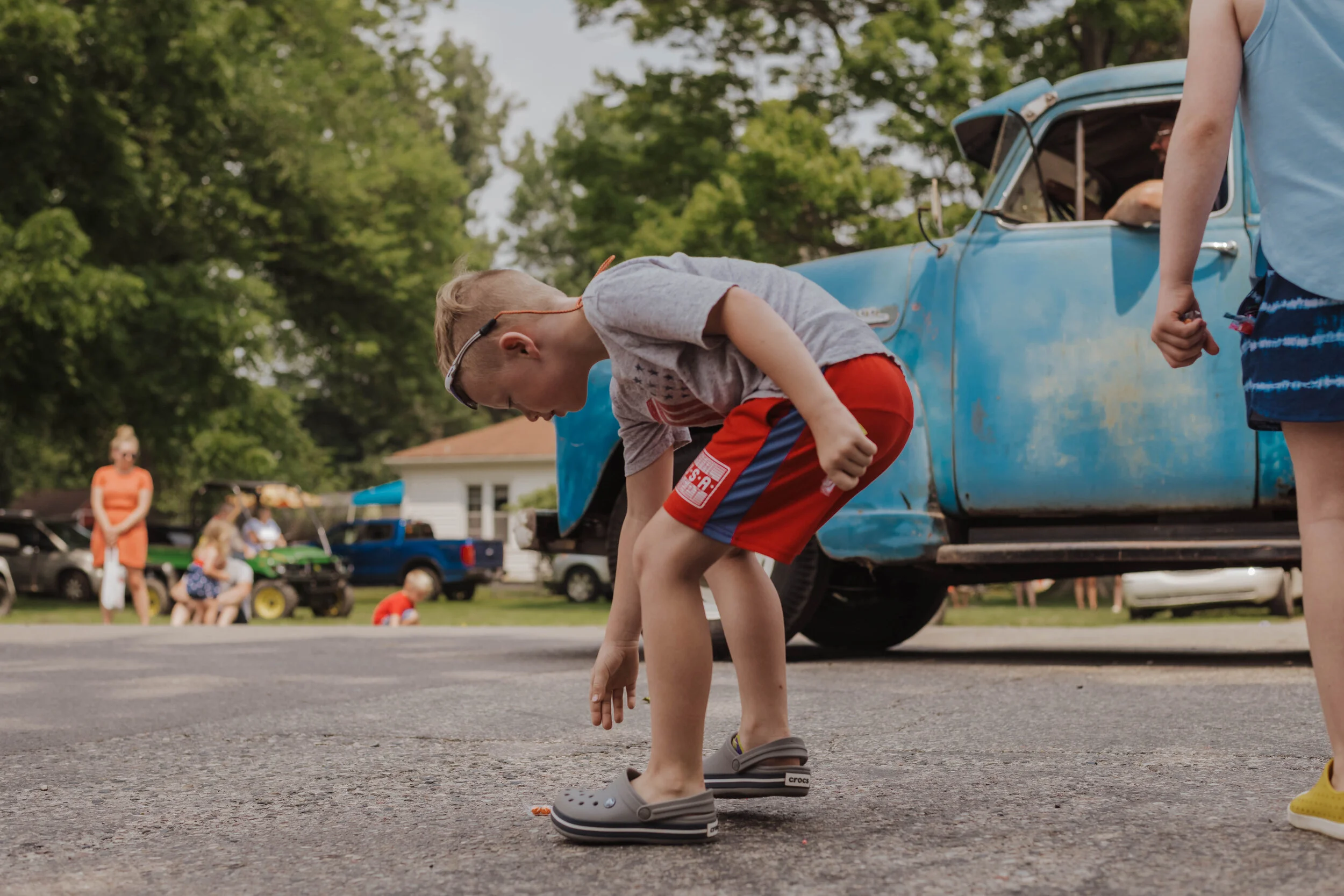 Candid photo of a boy picking up candy along a parade route during a family photography session by Forever Ago Photography. Capturing the joy and excitement of childhood in Irish Hills Michigan with authentic, timeless imagery