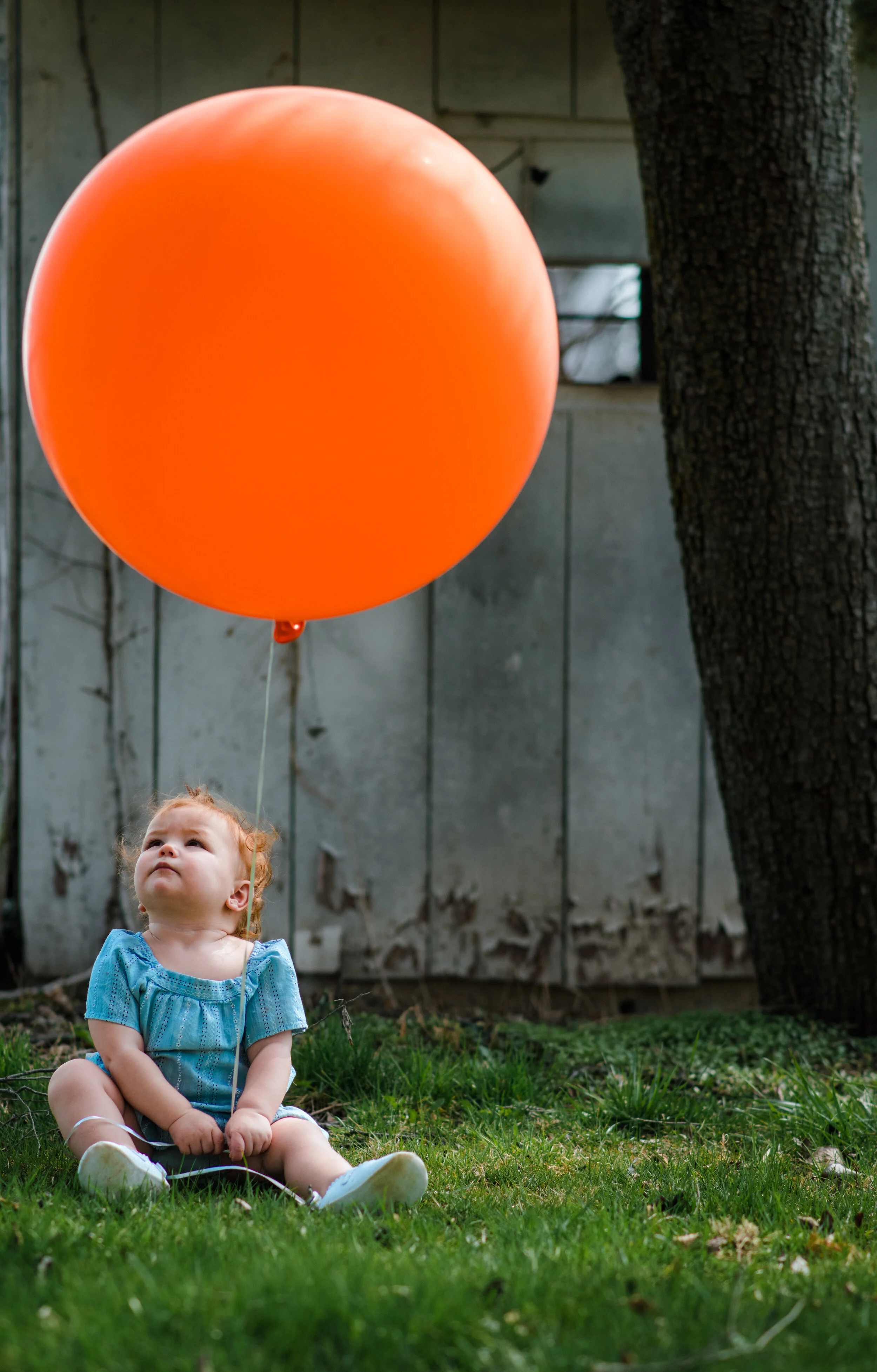 Candid photo of a child holding an orange balloon during a family photography session by Forever Ago Photography. Capturing the joy and wonder of childhood with authentic, timeless images in Carleton Michigan
