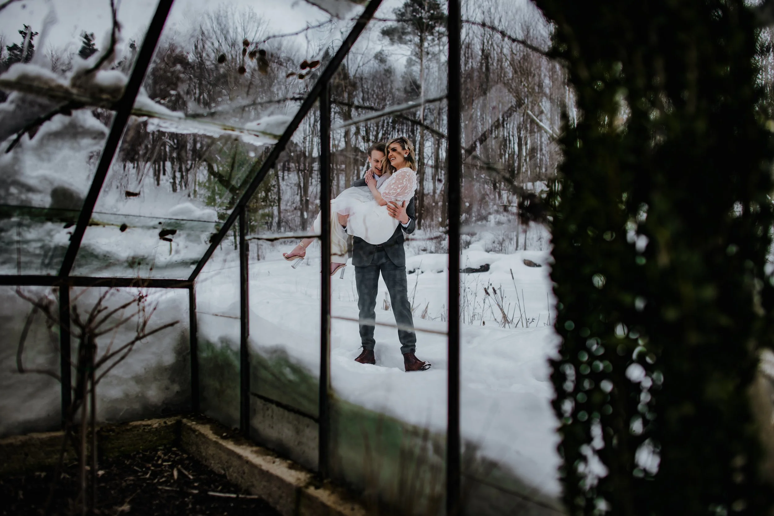 Dreamy image of a groom carrying his bride in a winter wedding greenhouse setting, captured by Forever Ago Photography in Trenton Michigan