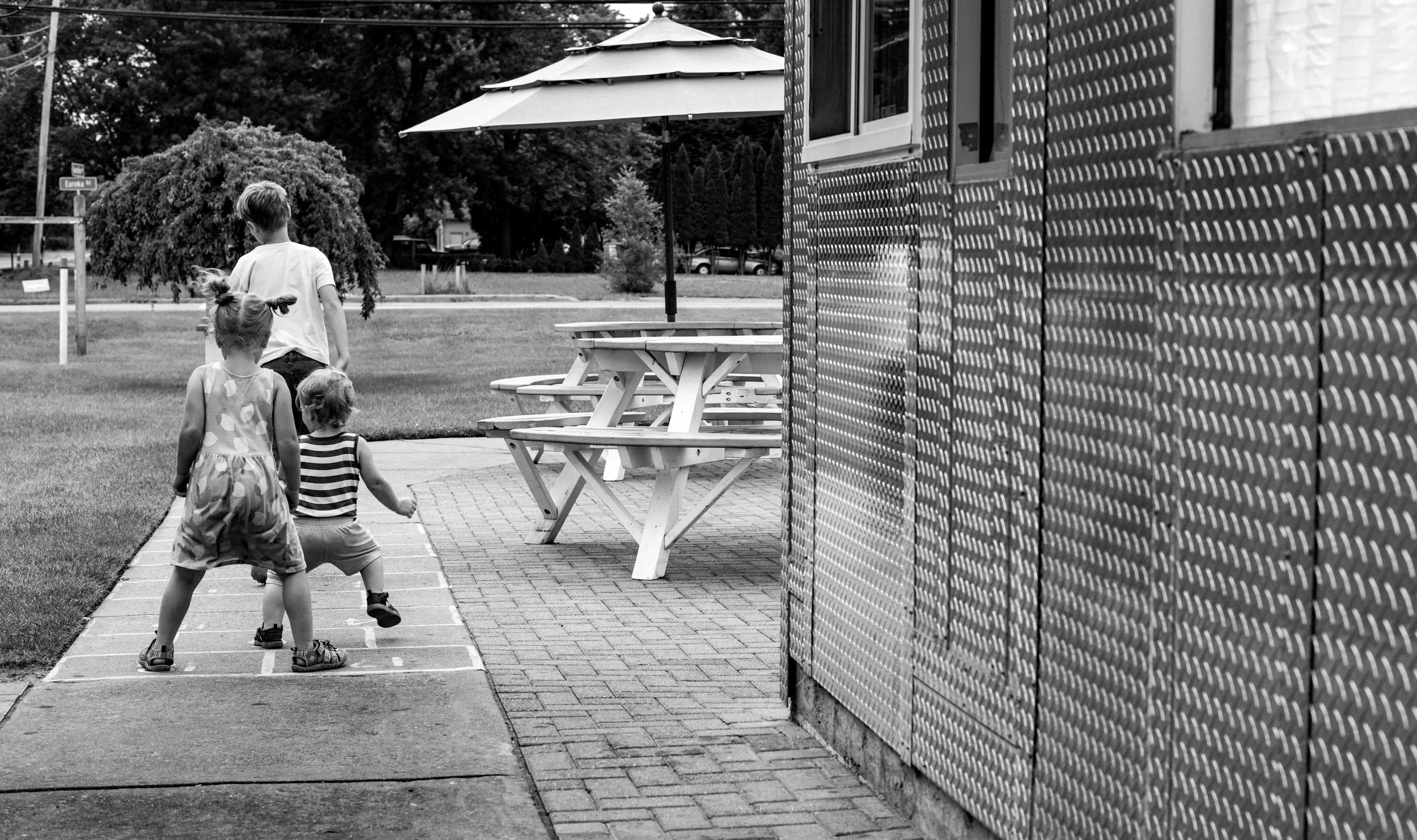 Candid photo of kids playing hopscotch during a family photography session by Forever Ago Photography. Capturing authentic childhood moments that highlight joy, connection, and timeless family memories in New Boston Michigan