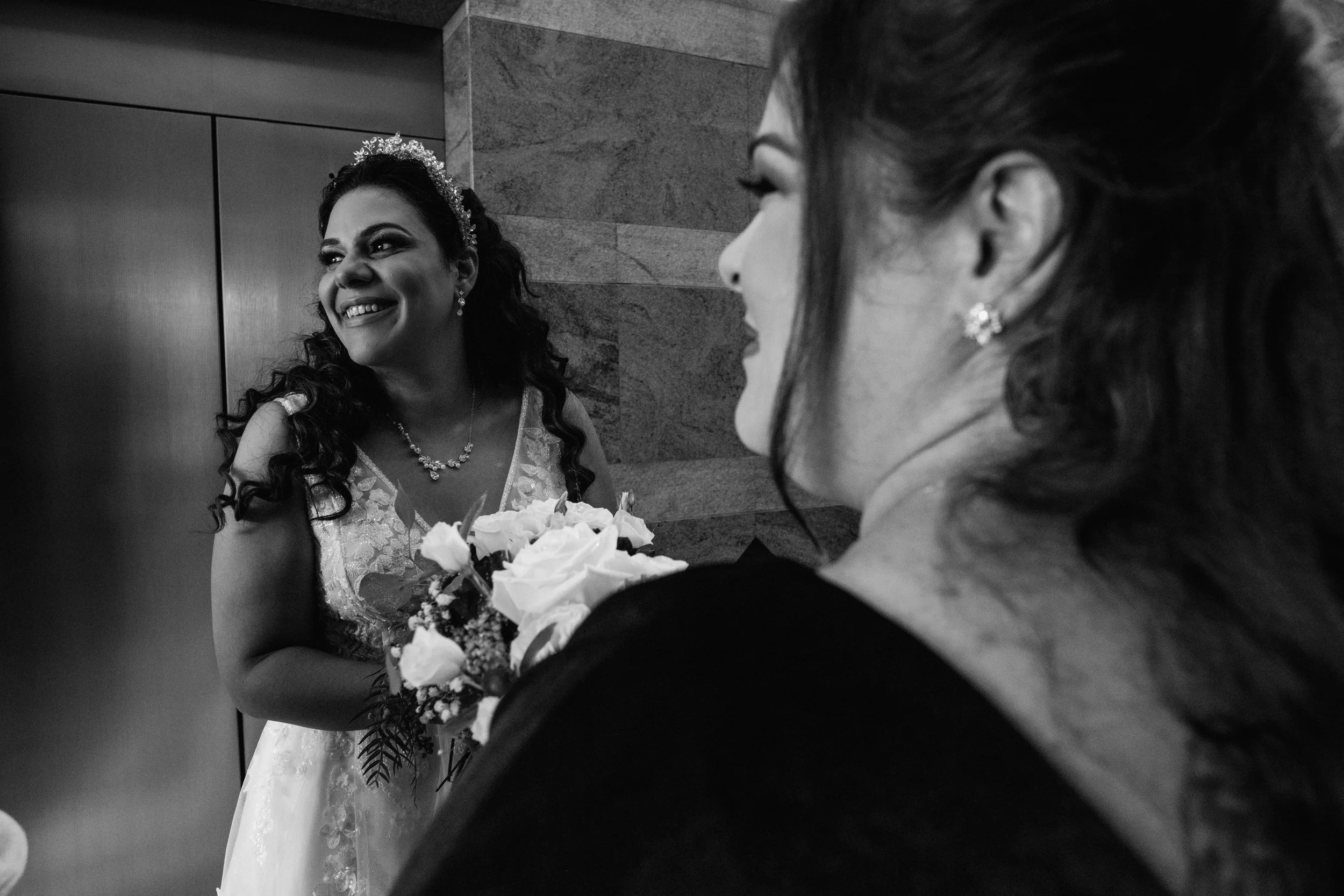Heartfelt black and white photo of a bride sharing a laugh with her bridesmaid after the wedding ceremony, beautifully captured in a documentary-style by Forever Ago Photography in Pontiac Michigan