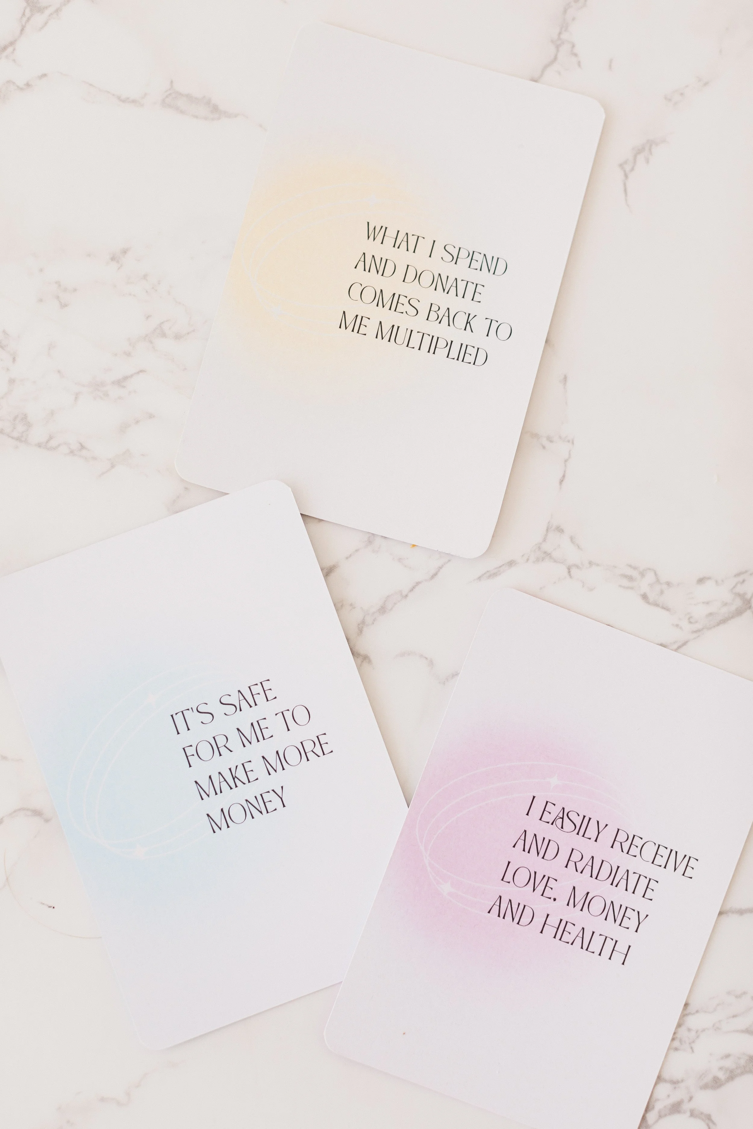 Cards with motivational and positive messages on a marble surface. The visible card reads, "What I spend and donate comes back to me multiplied."