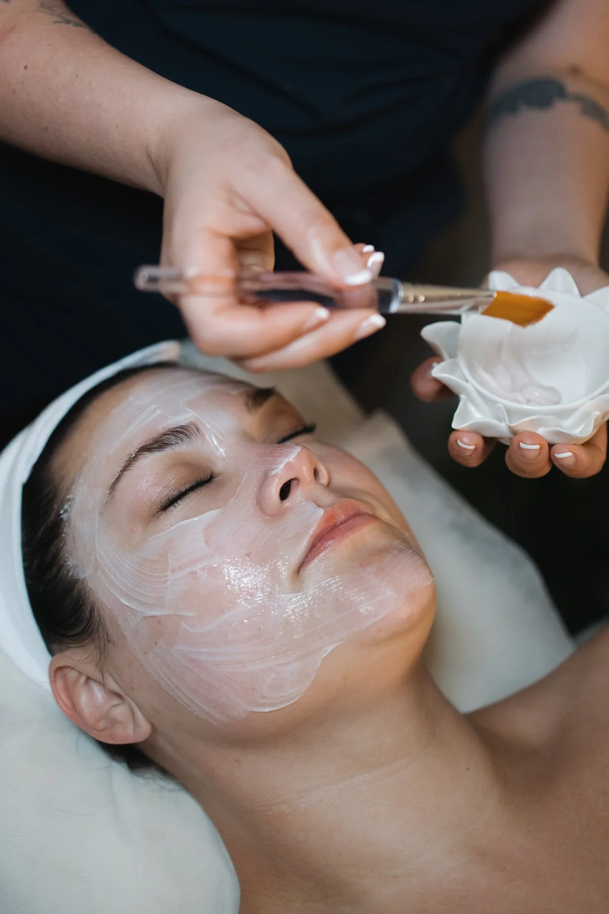 A woman receiving a buccal facial massage and skincare treatment in St. Louis, Missouri (located in Brentwood, MO) with a white mask being applied by an esthetician using a brush.