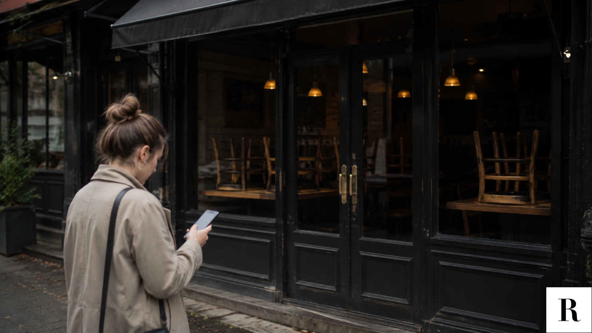 a woman staring at her phone in front of a closed restaurant.
