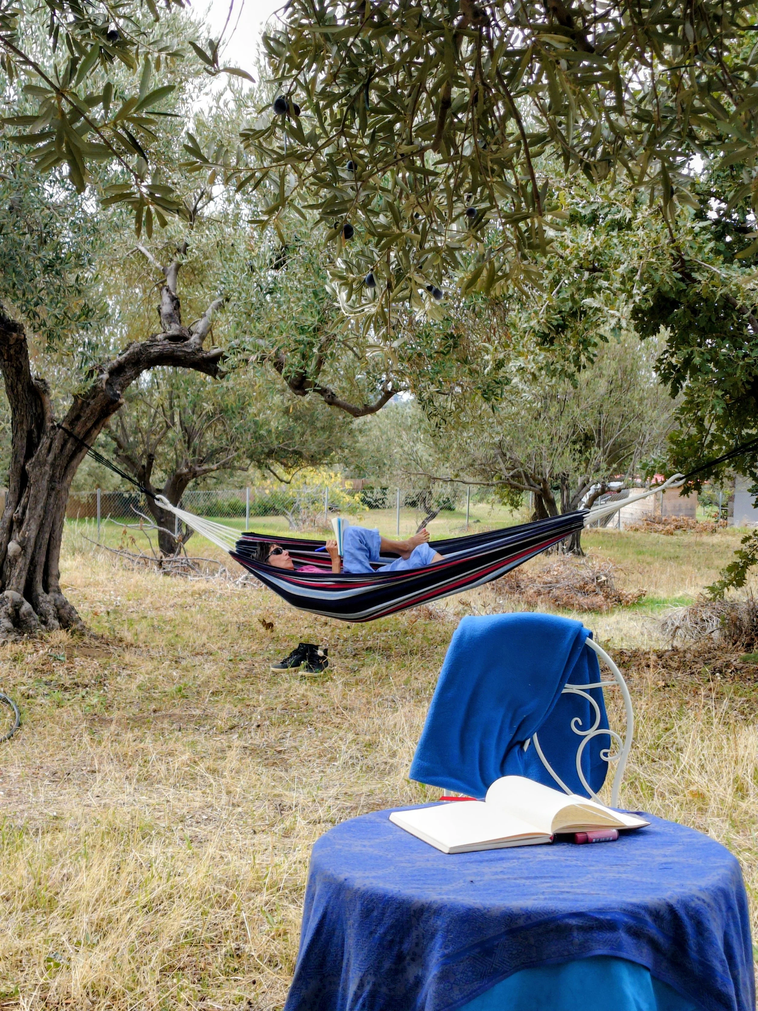barefoot woman writing, in a hammock, with a table and notebook in the foreground