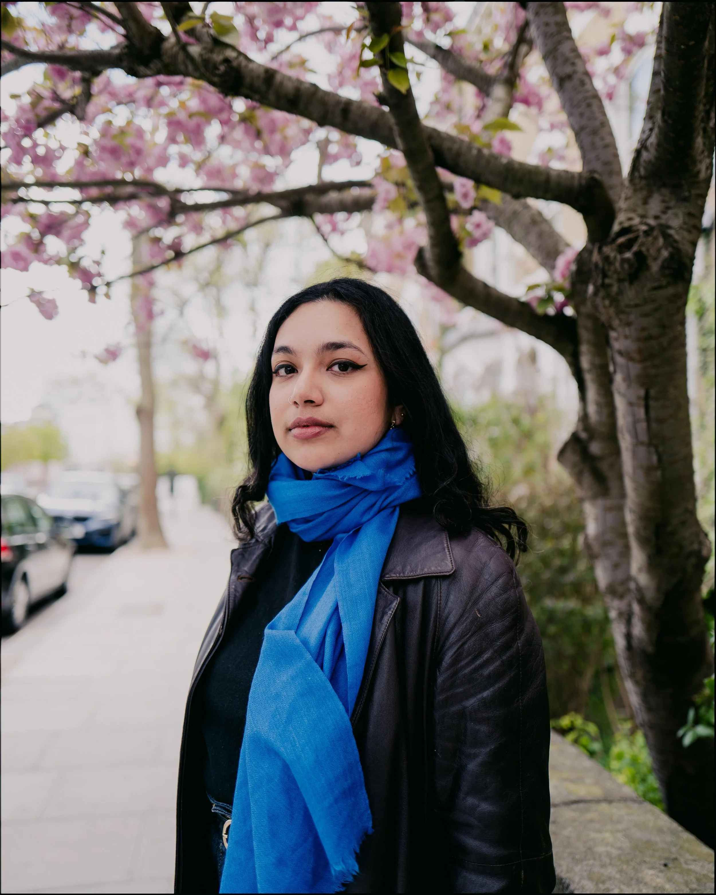 Girl with blue scarf and leather jacket with cherry blossoms in the background Vamika Sinha
