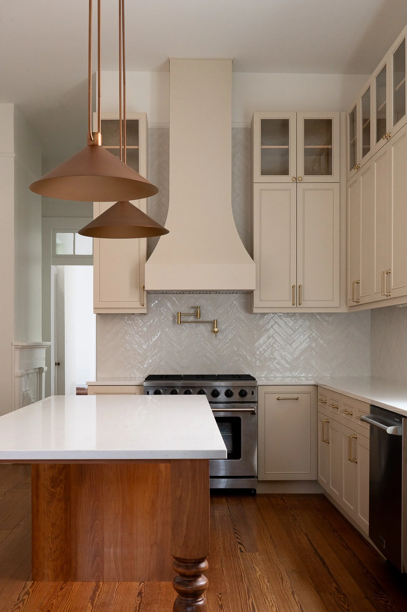 Modern kitchen with white cabinets, a stainless steel oven, a white countertop island, wood flooring, and copper pendant lights.