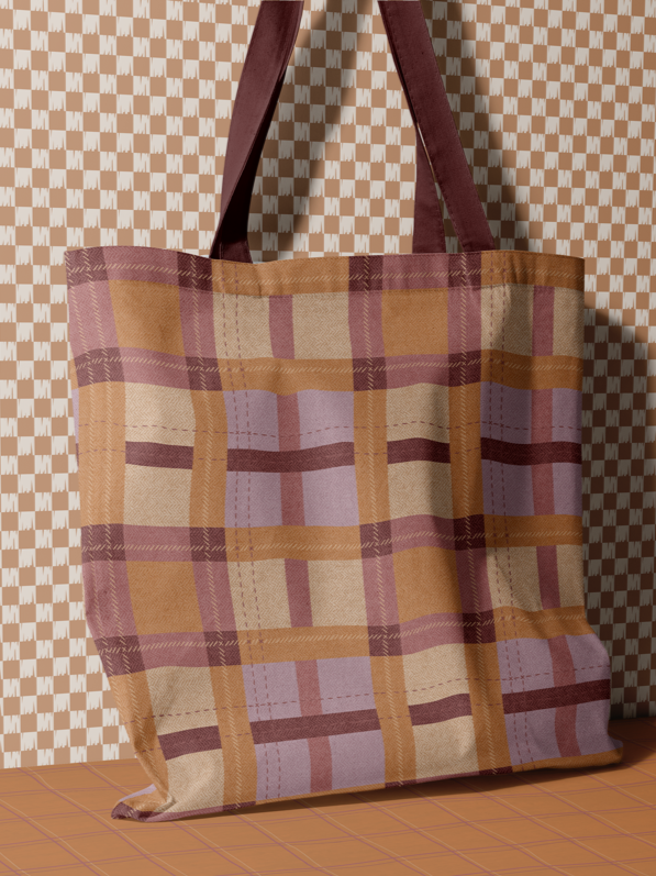 Plaid tote bag in burgundy, tan, and mauve against a checkered fabric backdrop