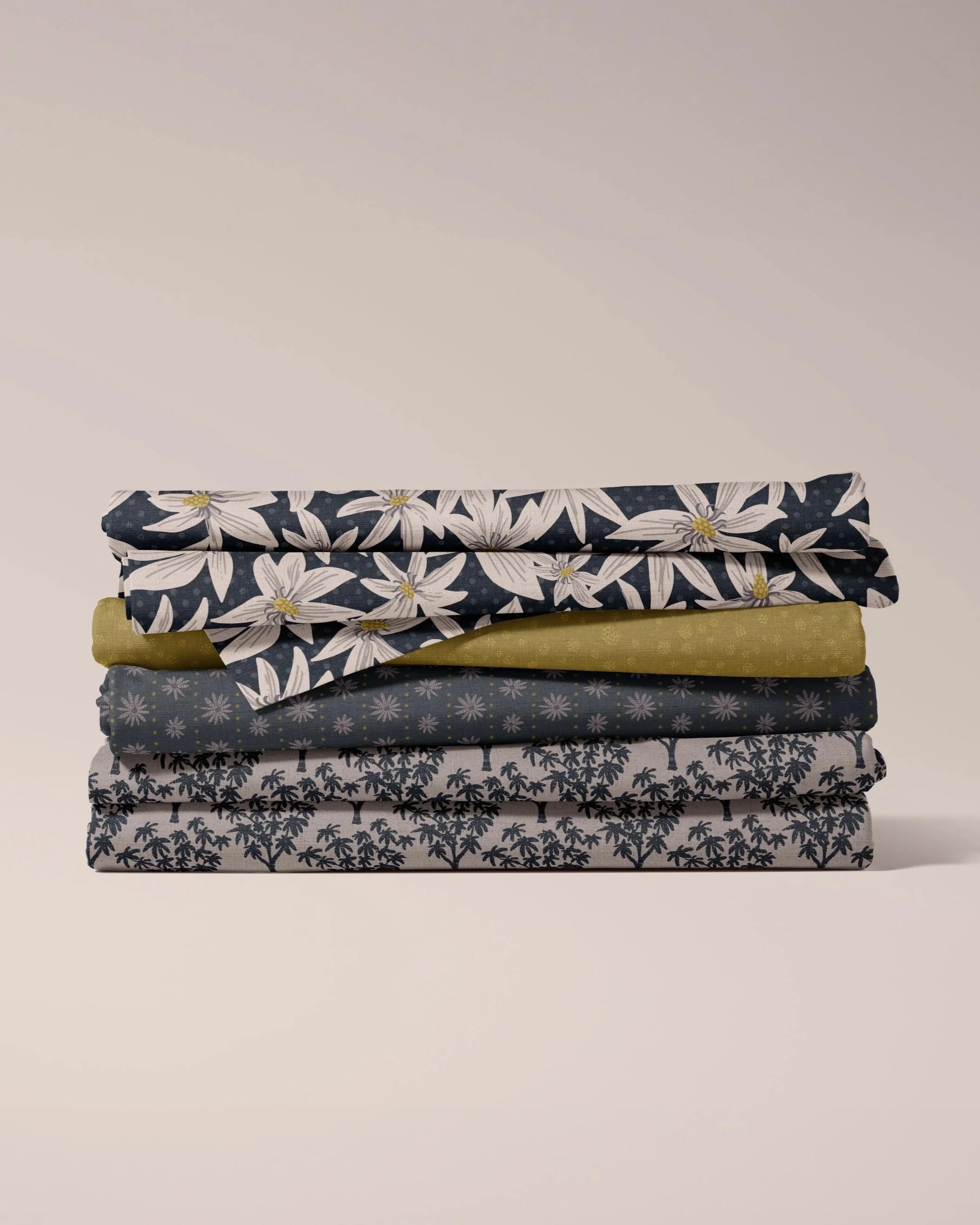 Stack of folded fabric bolts in floral, geometric, and palm print patterns in navy, olive, and gray