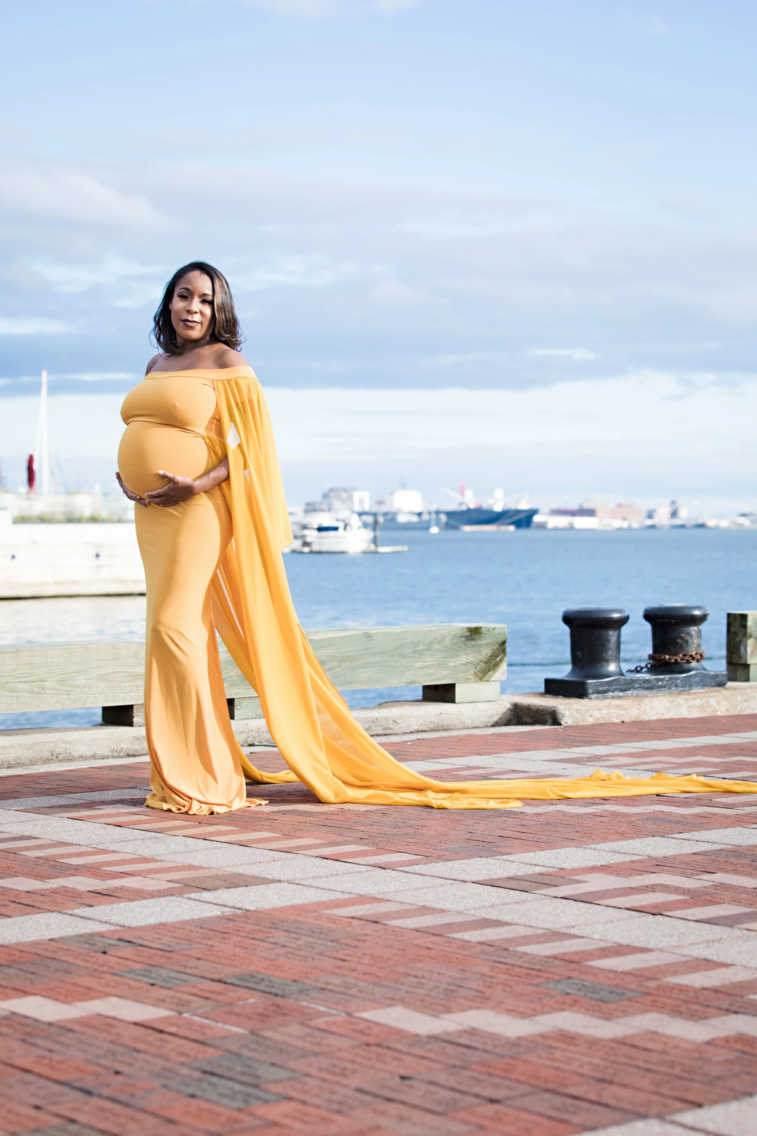 Pregnant woman in yellow dress posing by waterfront