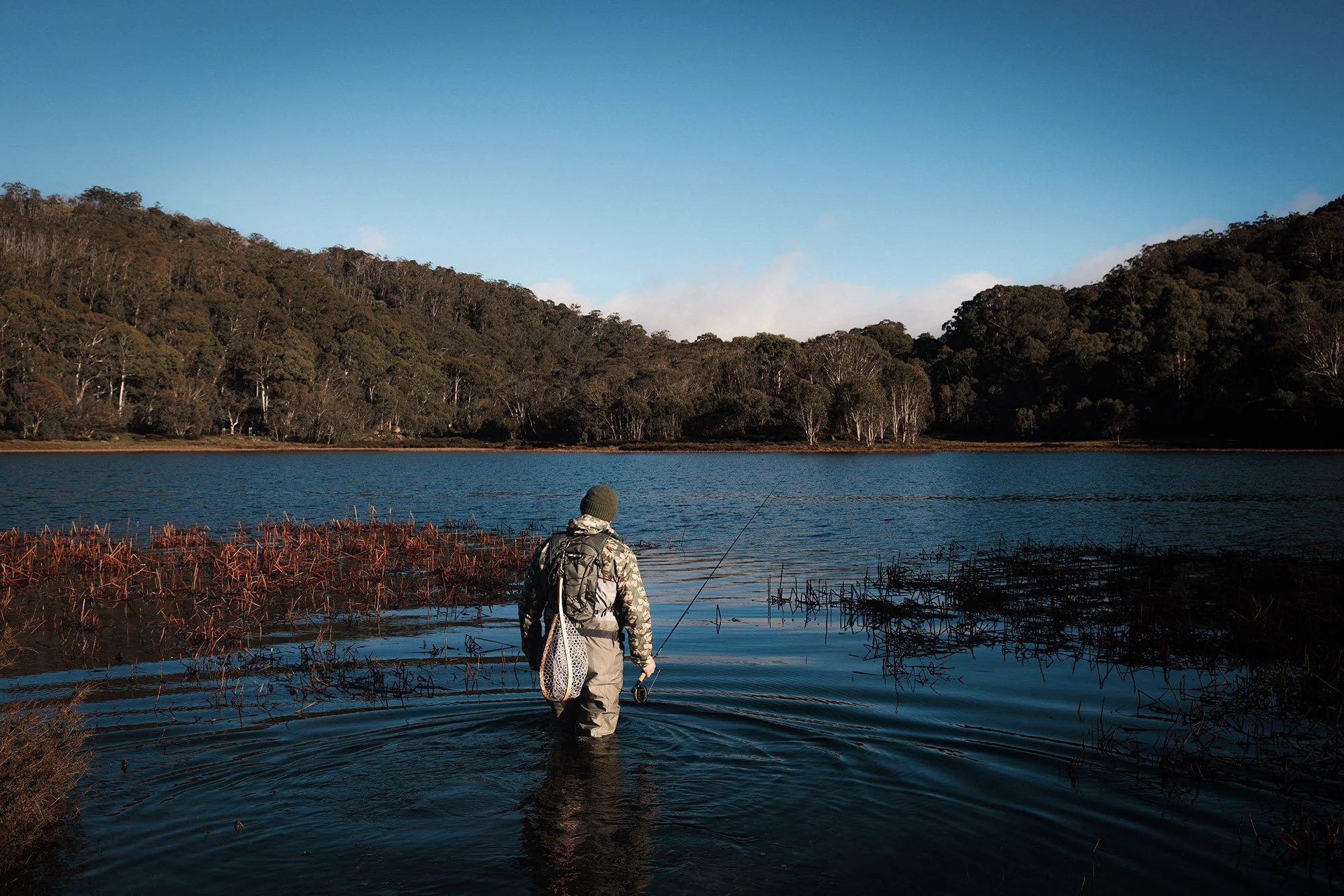 man wading in to lake with fly fishing gear