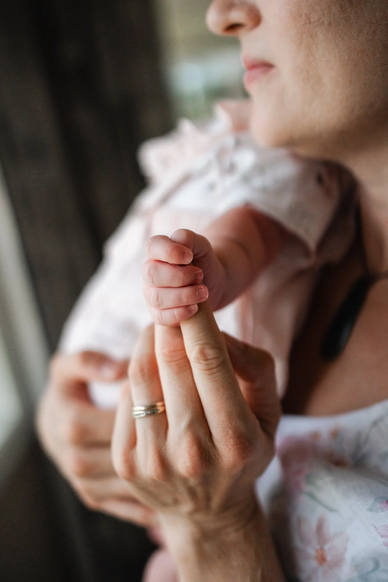 Close up photo of a newborn baby holding her mothers finger. They are lit by soft window light