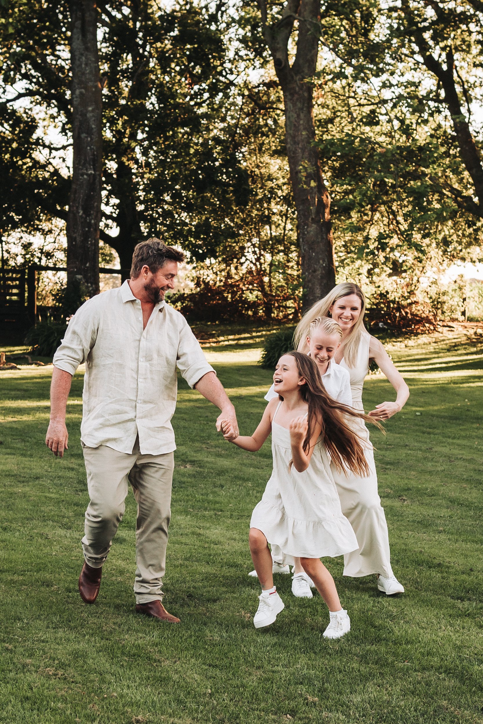 a family being playful with each other all dressed in cream for a family portrait in a private garden in Matamata