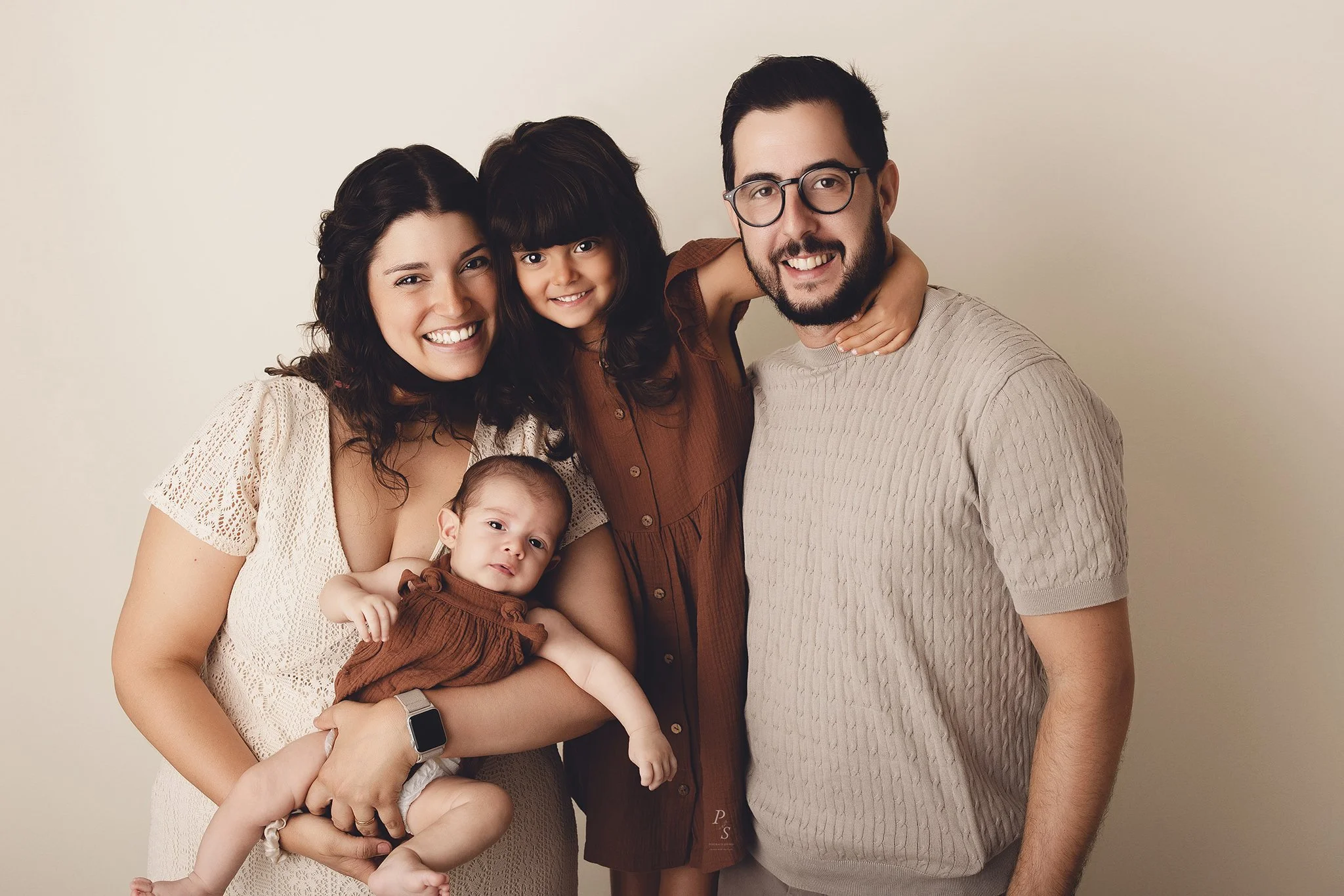 Família feliz com duas crianças, uma menina e uma bebê, sorrindo para a câmera contra fundo claro.  sessão fotográfica em estúdio no Porto