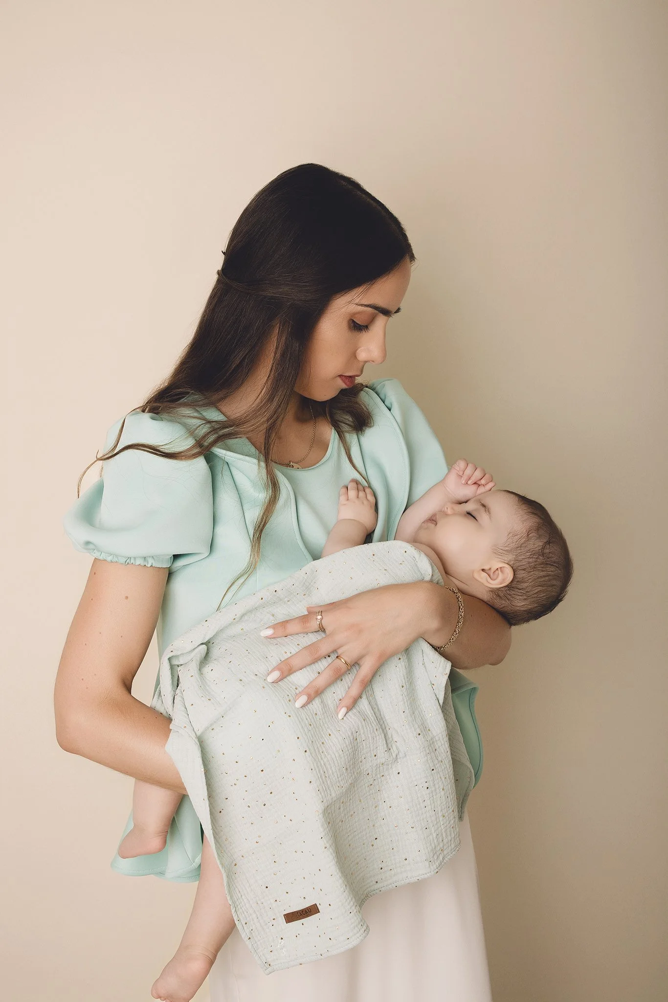 Mãe com bebé, que está deitado em seu colo, ambas com expressão de carinho e conexão. sessão fotográfica em estúdio no Porto