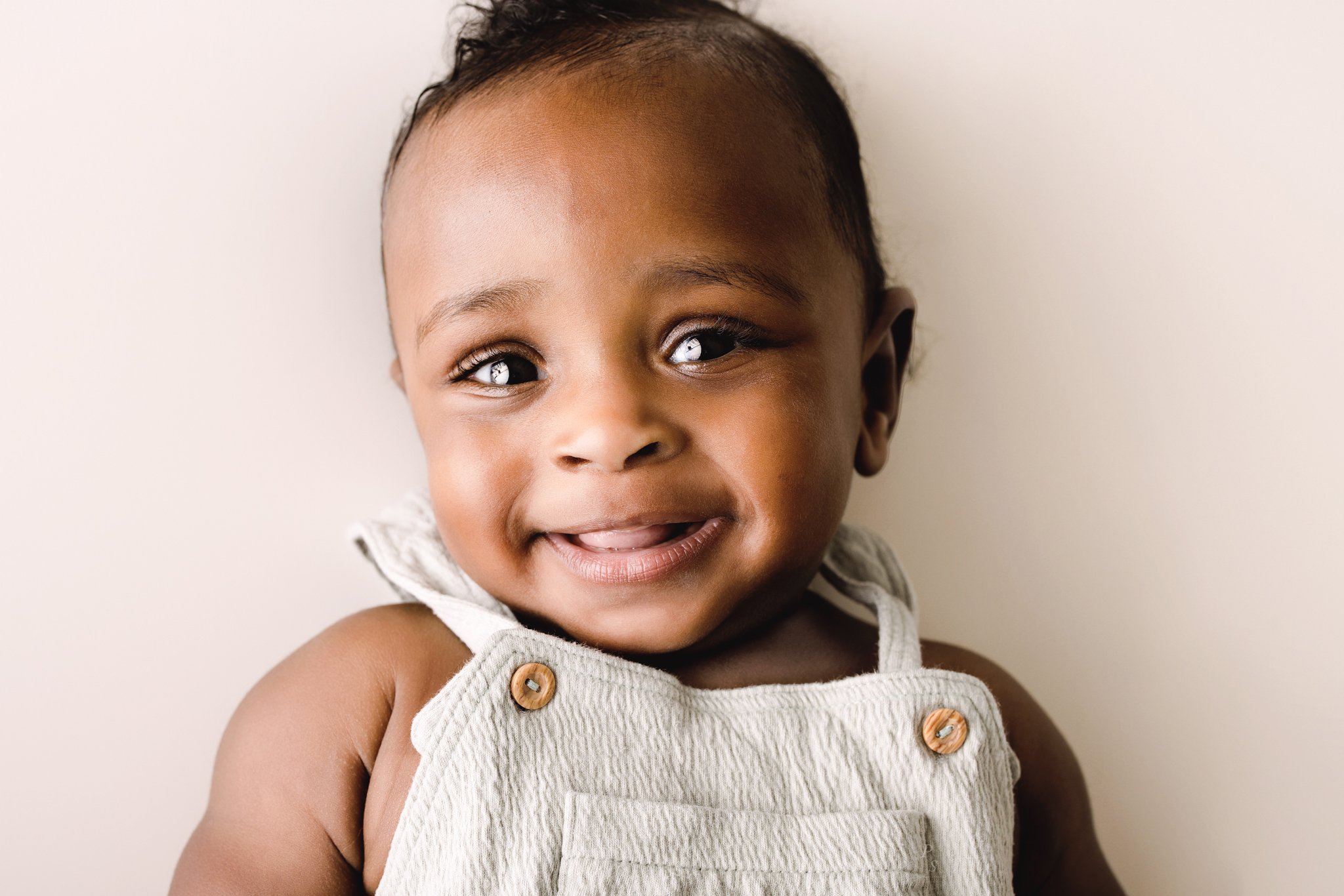 Bebé 6 meses sorridente, num fundo neutro. sessão fotográfica de família num estúdio do Porto.