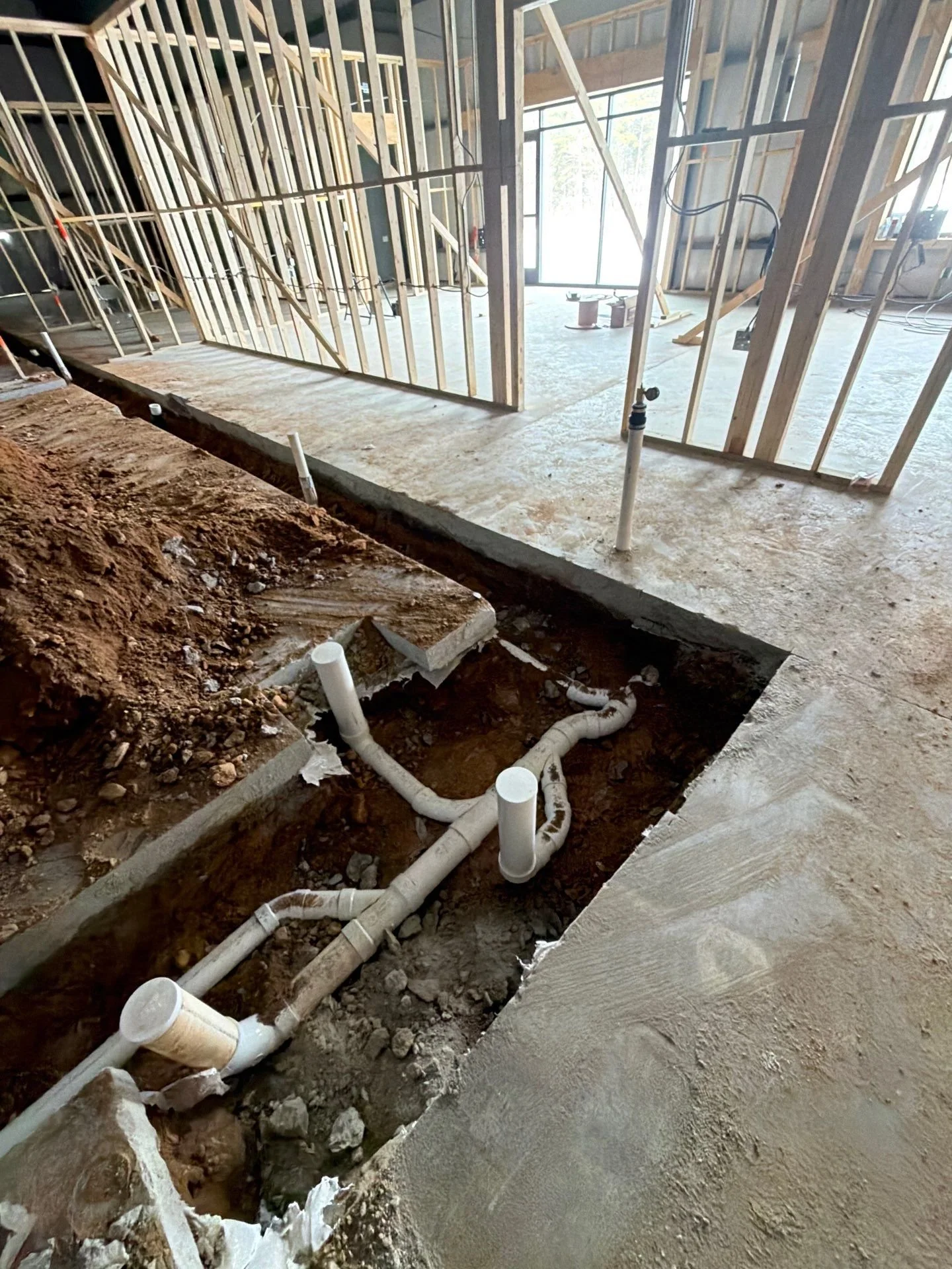 Construction site interior showing exposed plumbing pipes and framing for walls and flooring.
