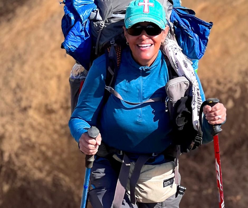  A woman in a blue long-sleeve shirt, smiling as she hikes uphill 