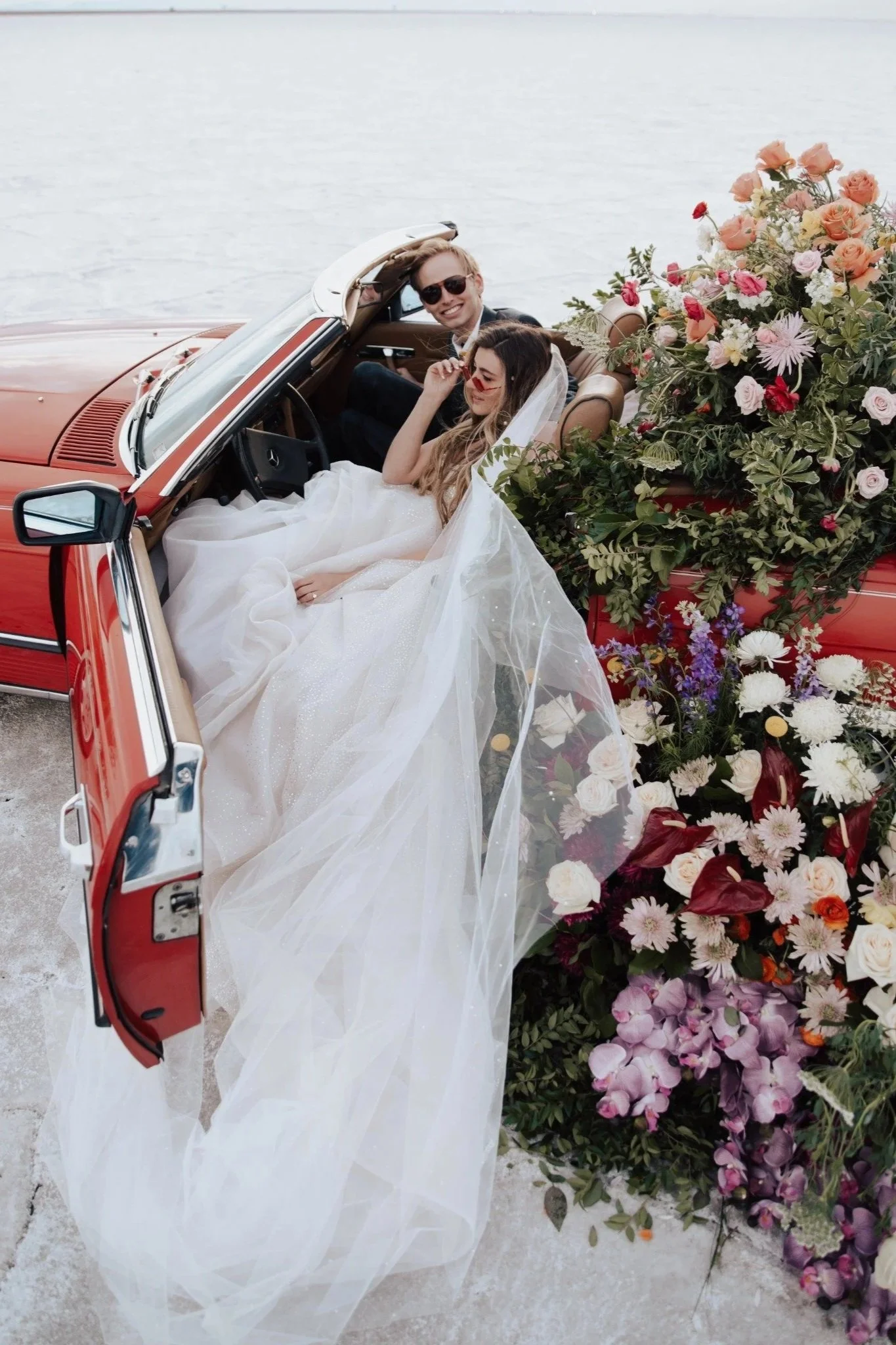 Red vintage car with florals and a bride and groom sitting in the front.jpg