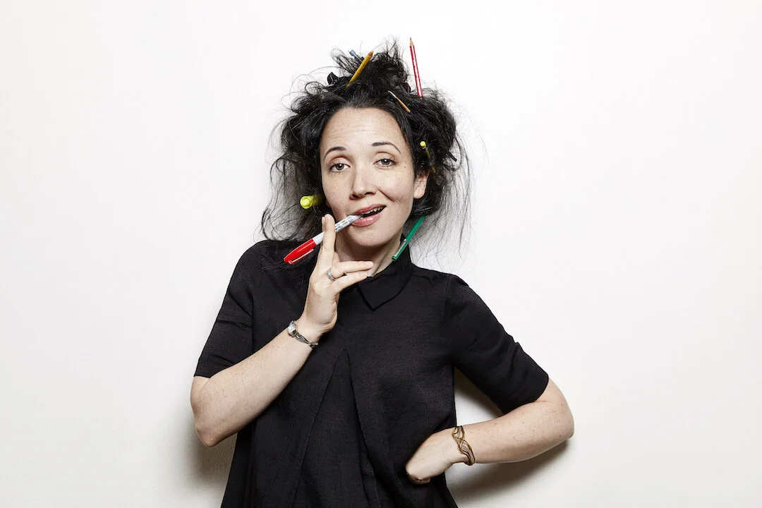 Freelance health content marketing writer Jacqueline Raposo stands smiling into the camera with pens and markers stuck in her messy hair, mock-smoking a Sharpie.