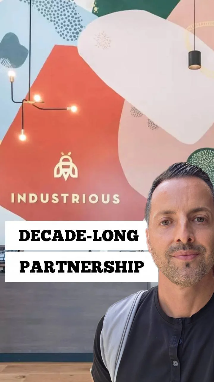 George Stroumboulis beside an Industrious mural in Seattle, with the words Decade-Long Partnership on the image.