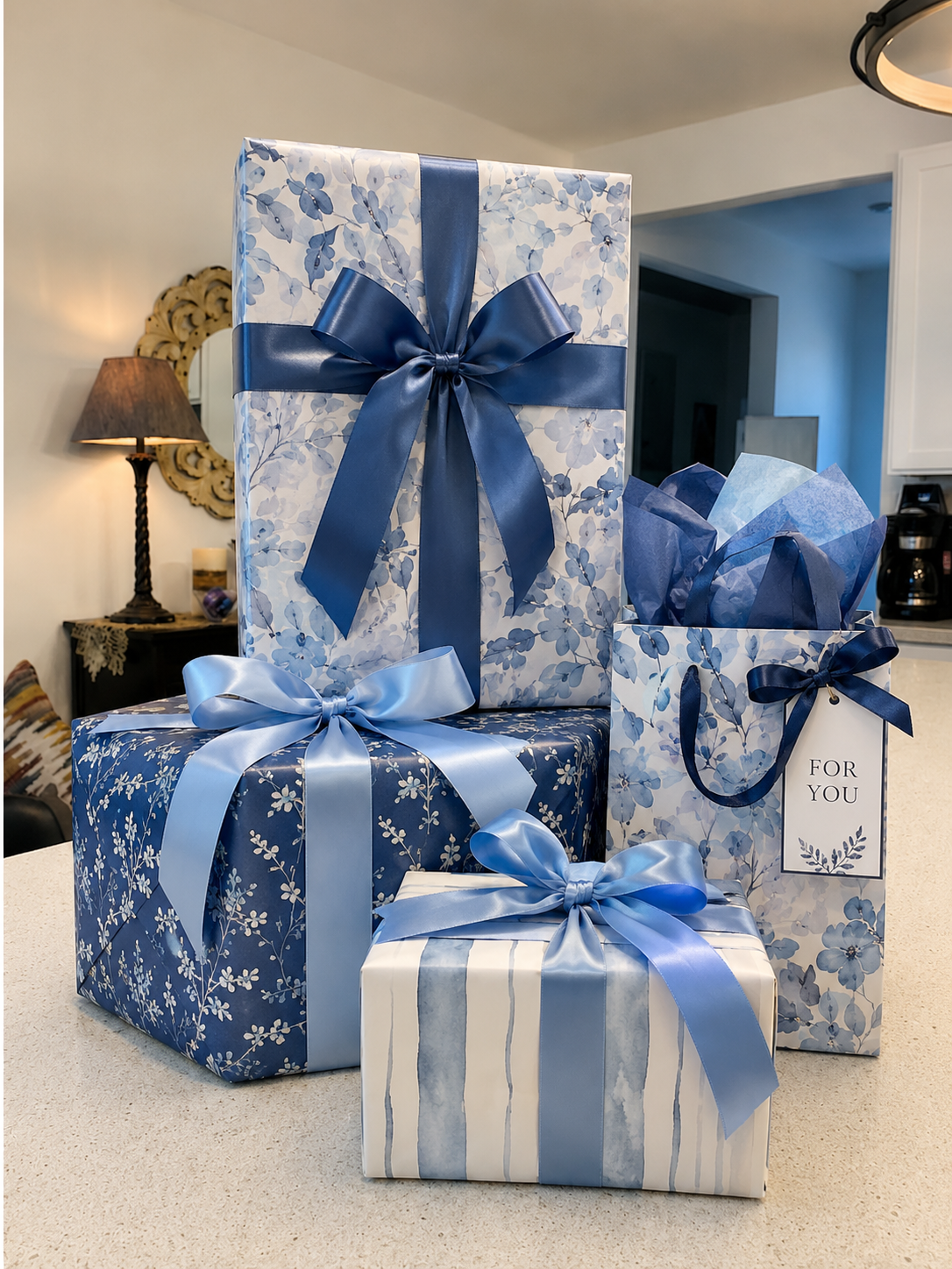 Four wrapped gift boxes with blue ribbons and floral paper, one with a 'For You' tag, placed on a kitchen countertop.